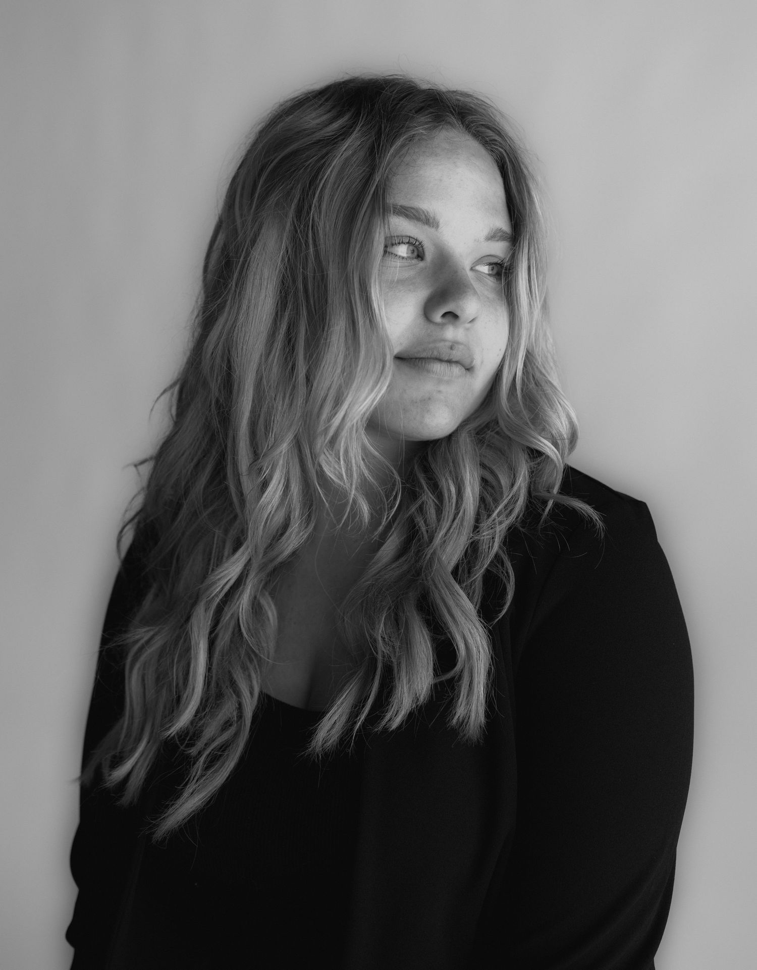 Black and white portrait featuring wavy blonde hair and a black blazer against a light background.