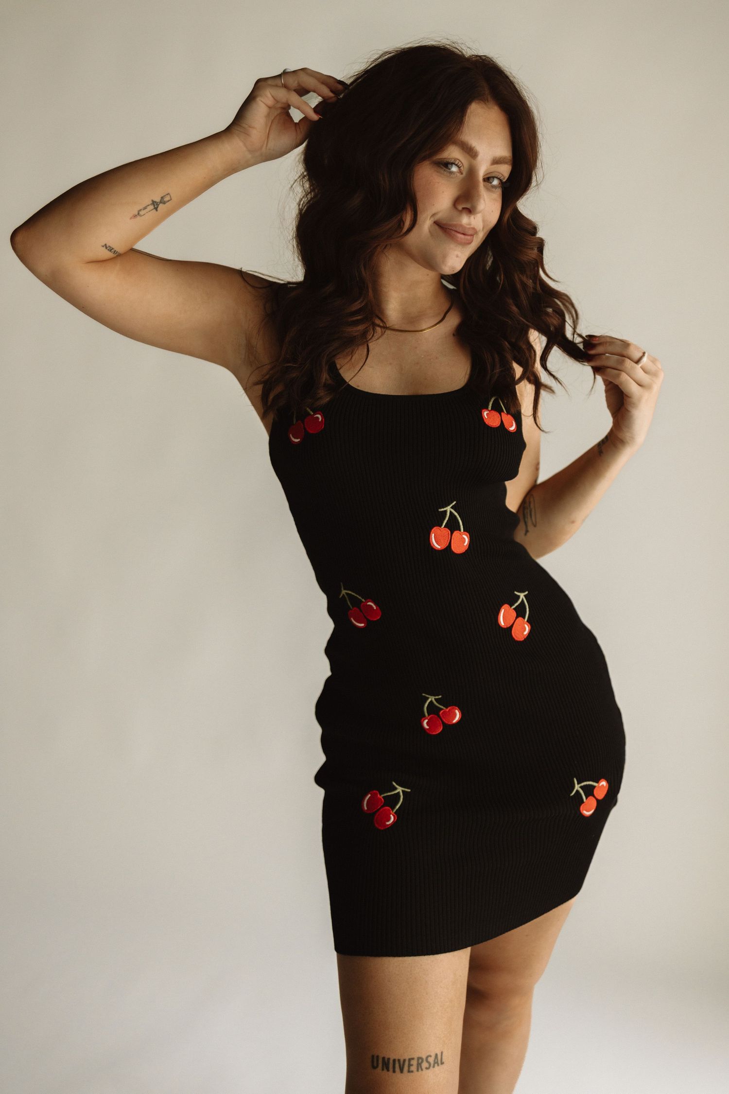 A black fitted dress adorned with red cherry embroidery details shown against a light beige studio background.