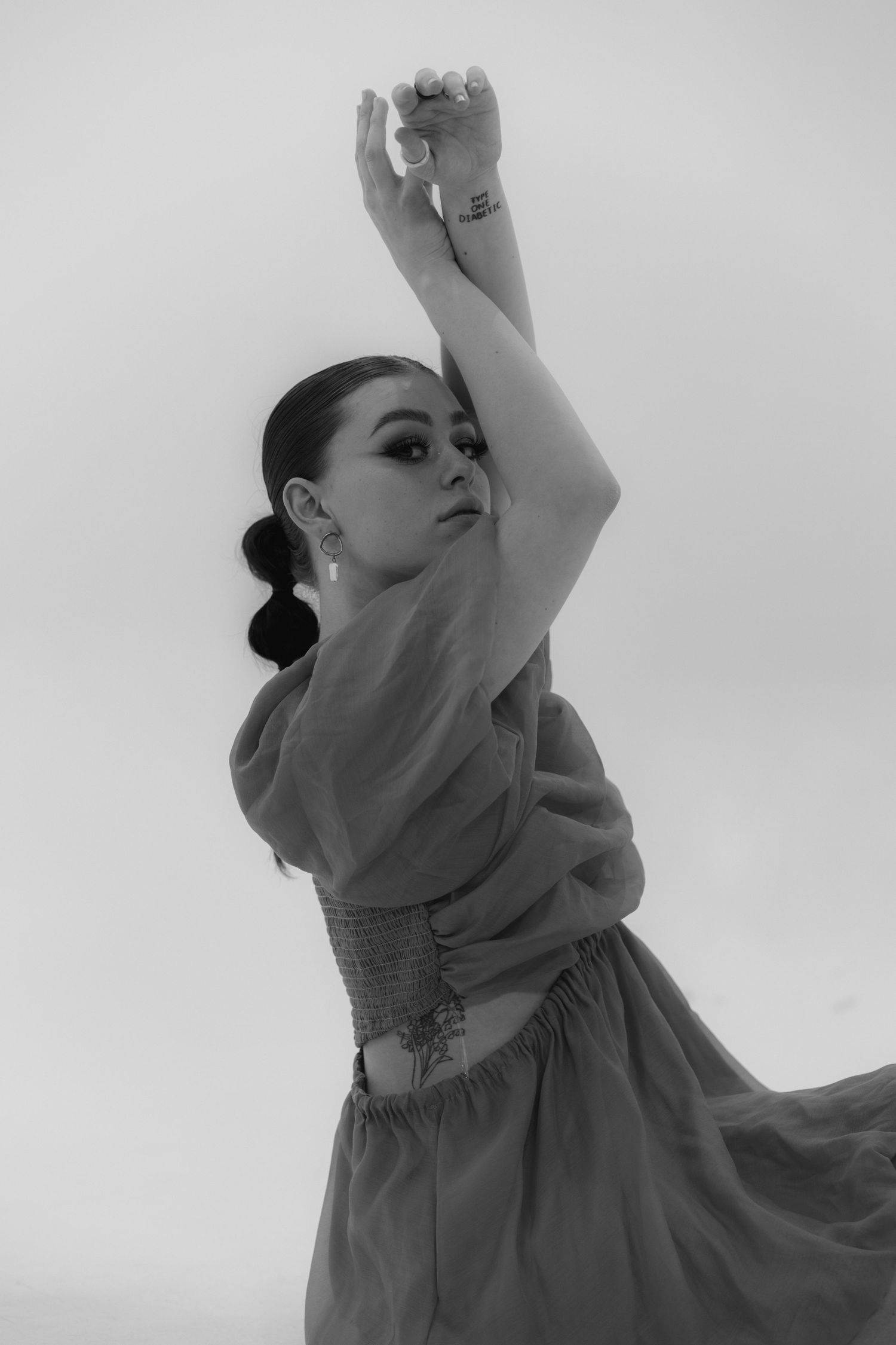 Black and white portrait of a dancer in an elegant dress striking a graceful pose with raised arms.