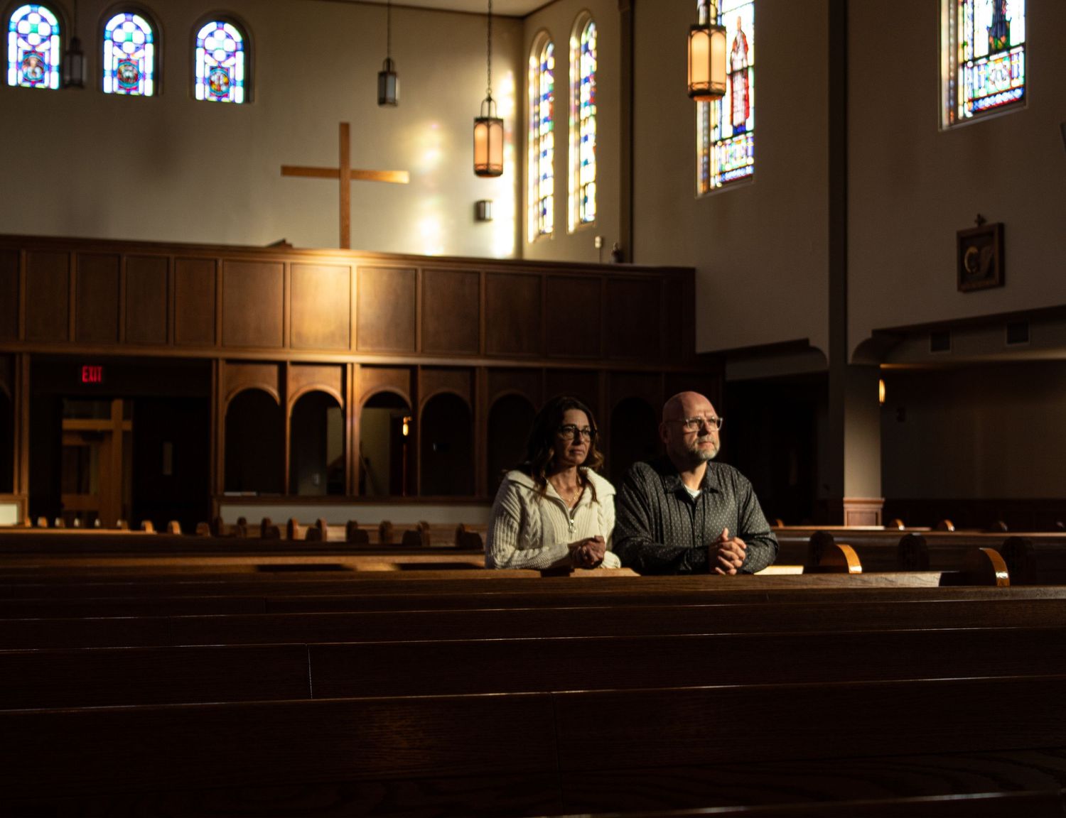 A dimly lit historic church interior with stained glass windows and wooden pews illuminated by hanging lanterns.