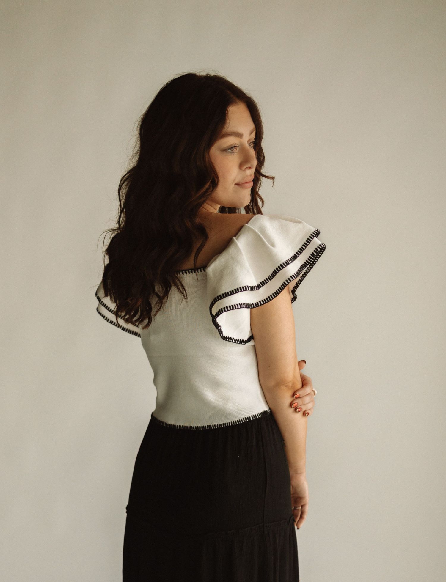 Portrait shot of someone wearing a white ruffle sleeve top and black skirt against a neutral backdrop.