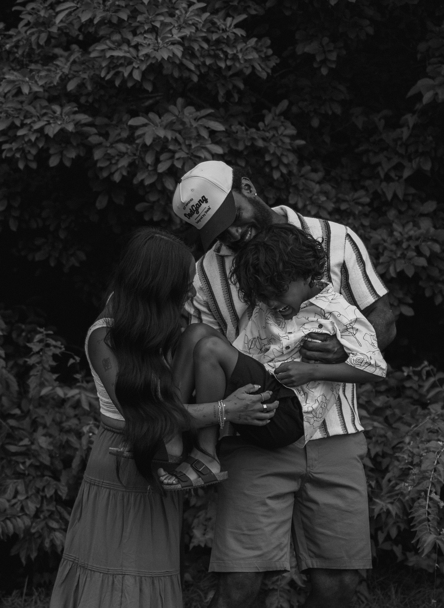 Four black and white photographs showing a romantic bond between two people in an outdoor setting with lush foliage.