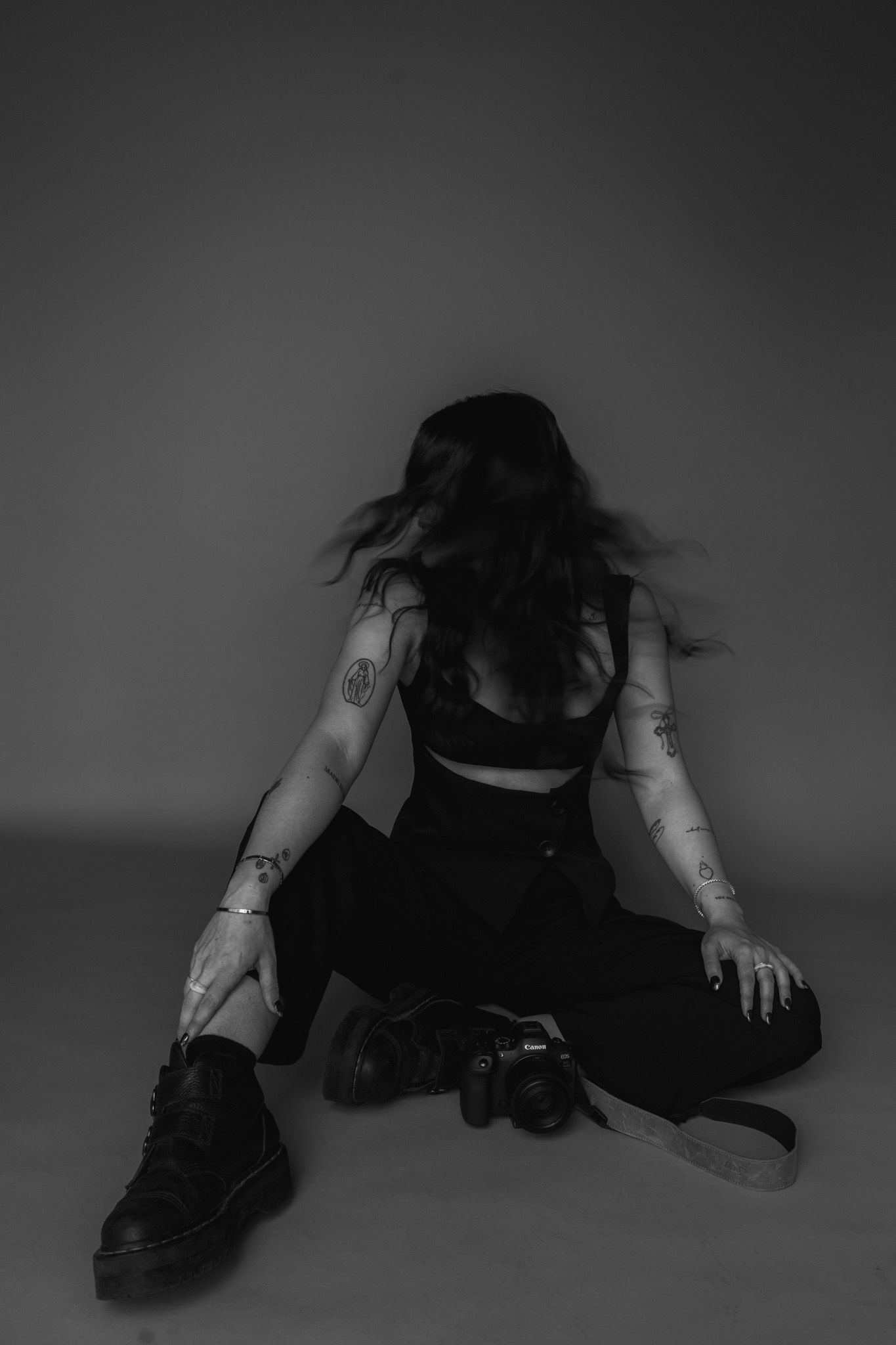 Moody black and white photo of photographer sitting with camera and visible tattoos.