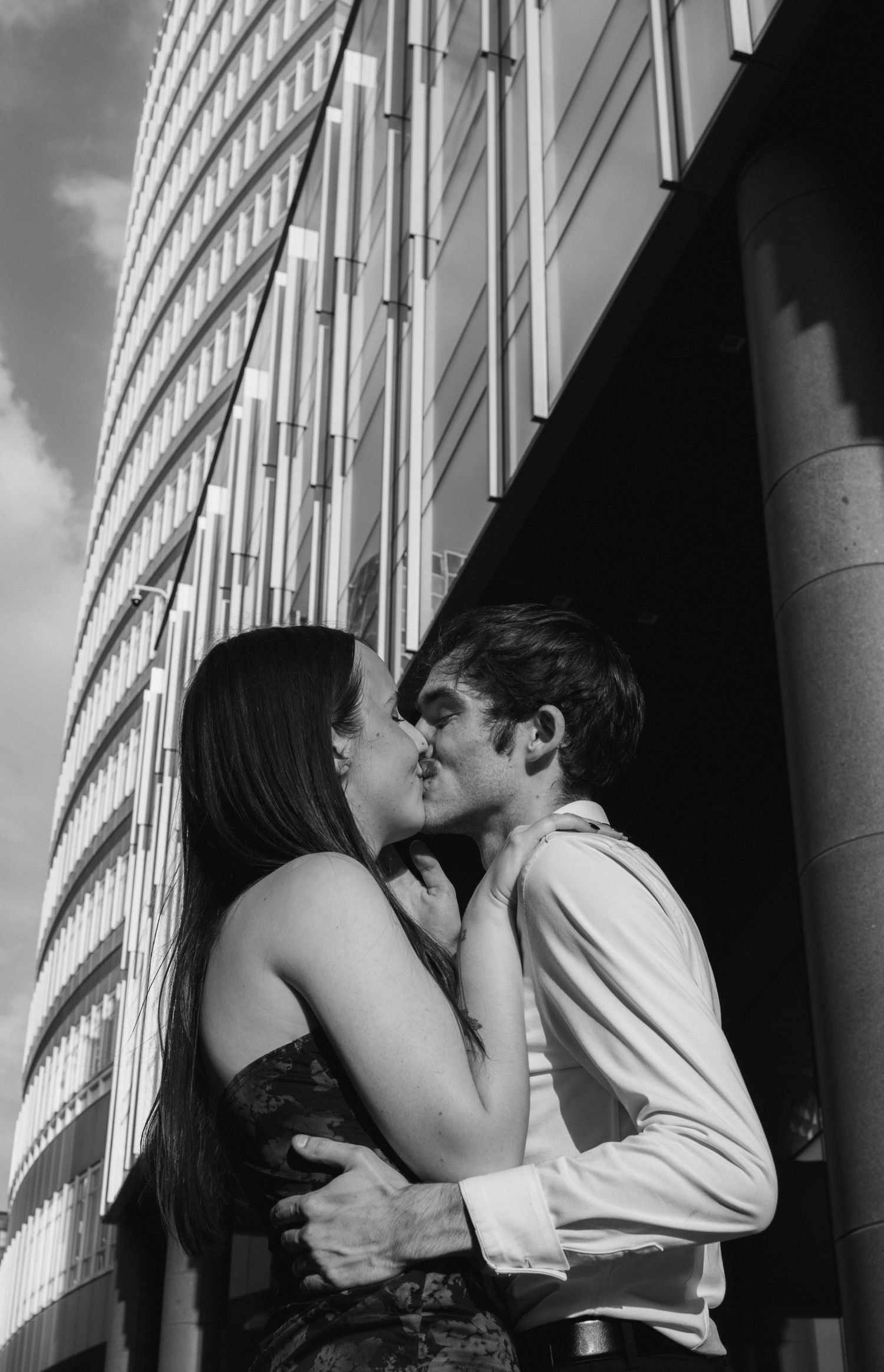 A romantic black and white photograph of a couple sharing a passionate kiss against a modern architectural backdrop.