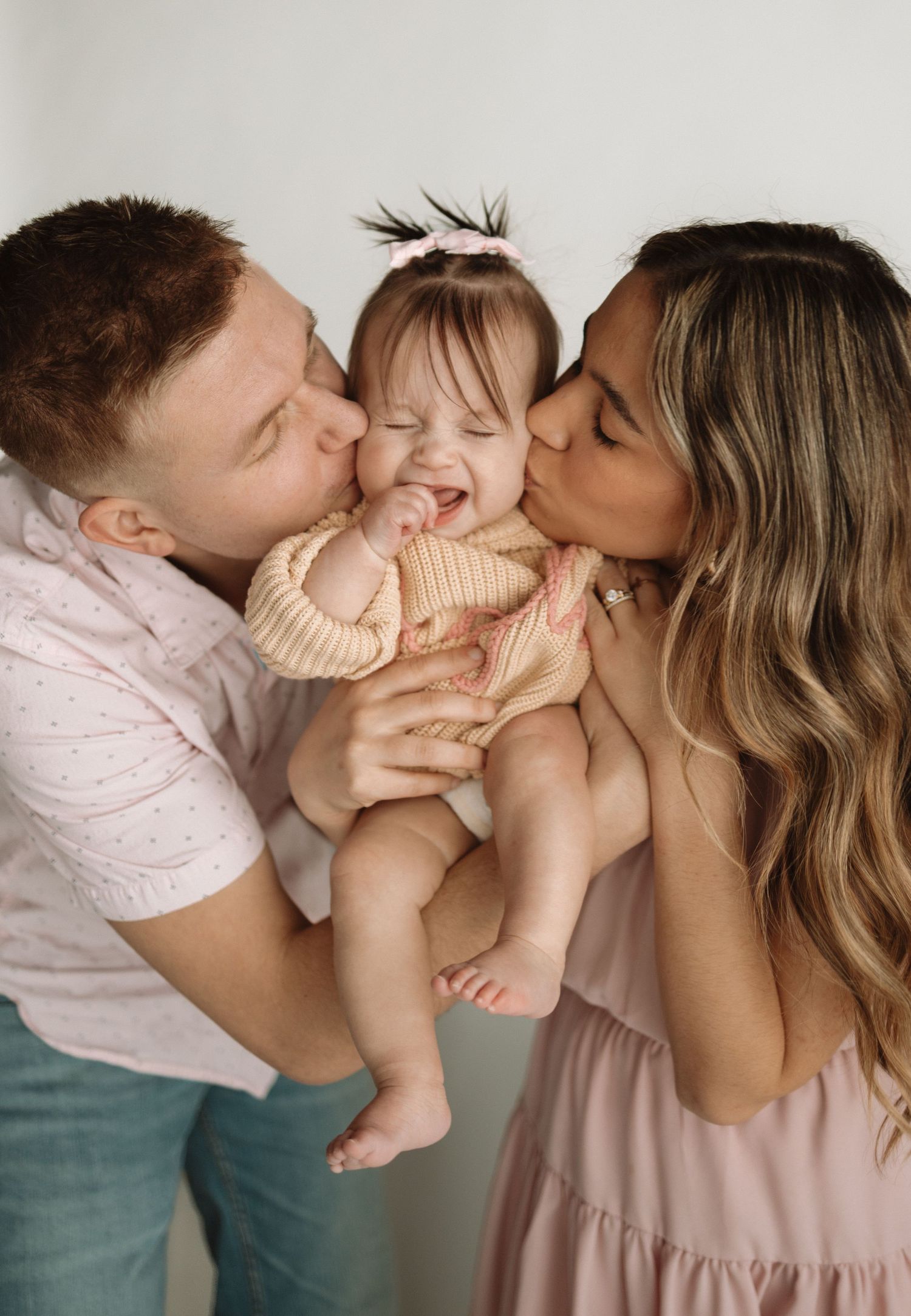 A tender family moment captured in a series of four connected photos showing parents kissing their baby's cheeks.