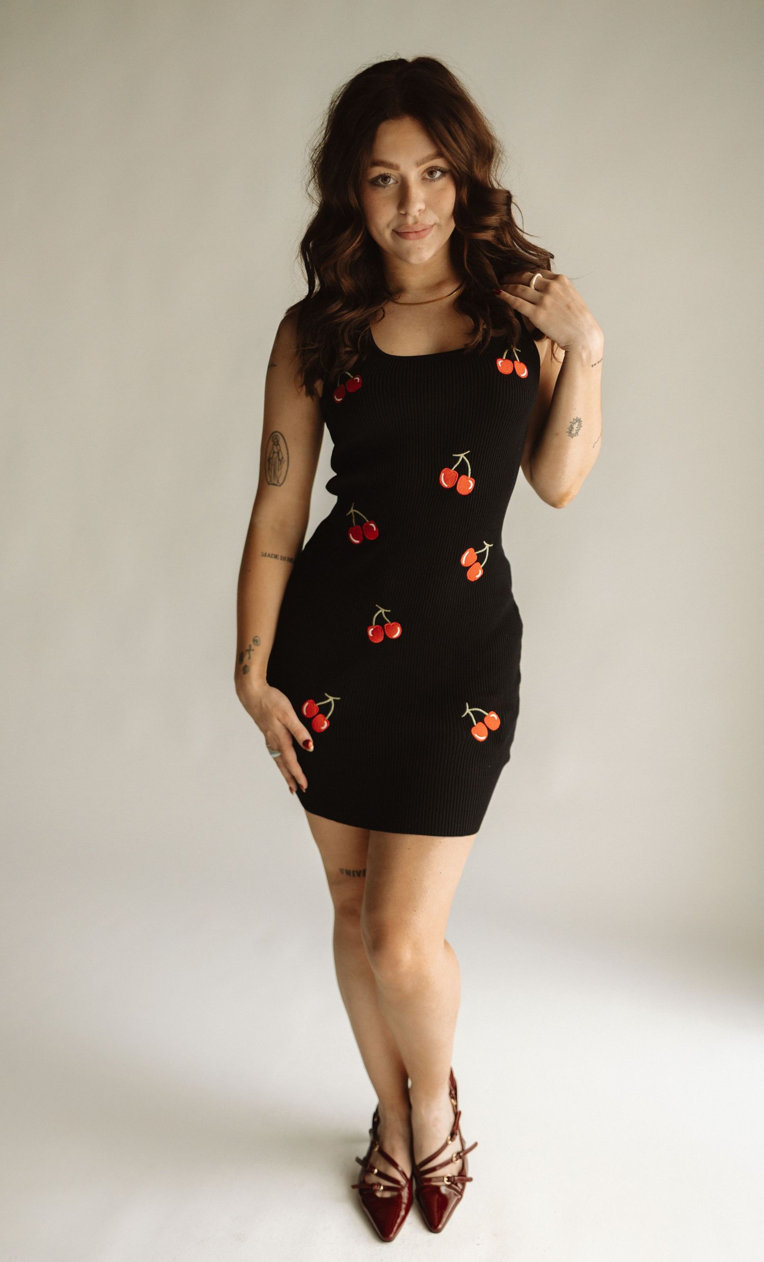 A stylish black tank top with cherry embellishments shown in multiple poses against a white background.