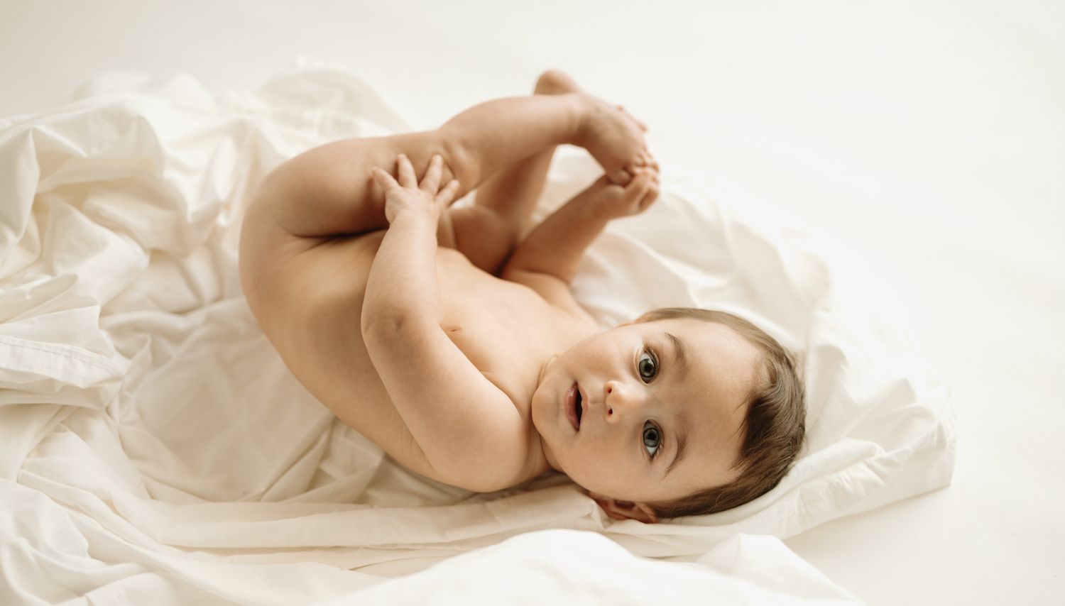 Baby lying on white fabric wearing light colored onesie.
