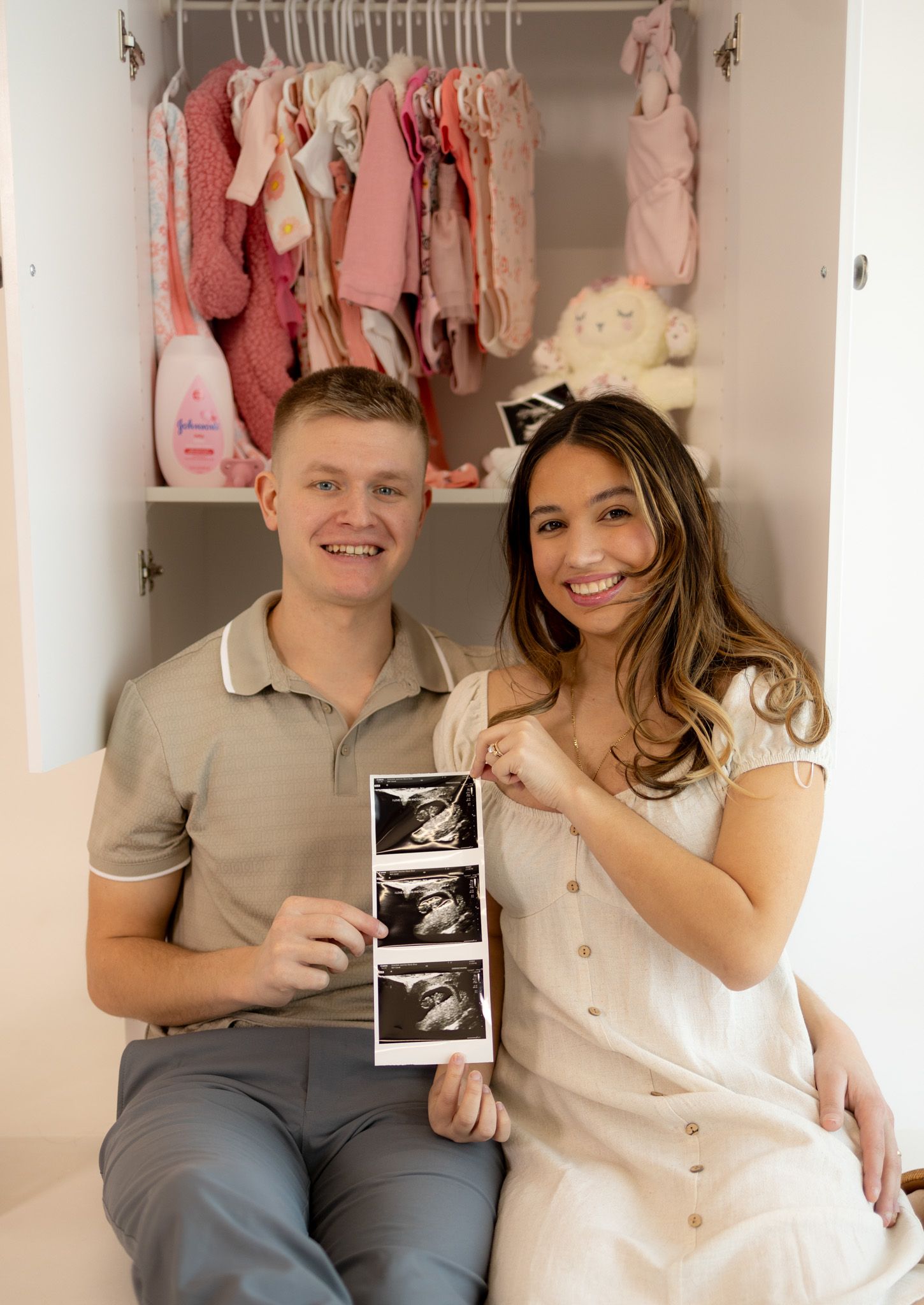 A pregnancy announcement photo showing ultrasound images with baby clothes hanging in the background closet.