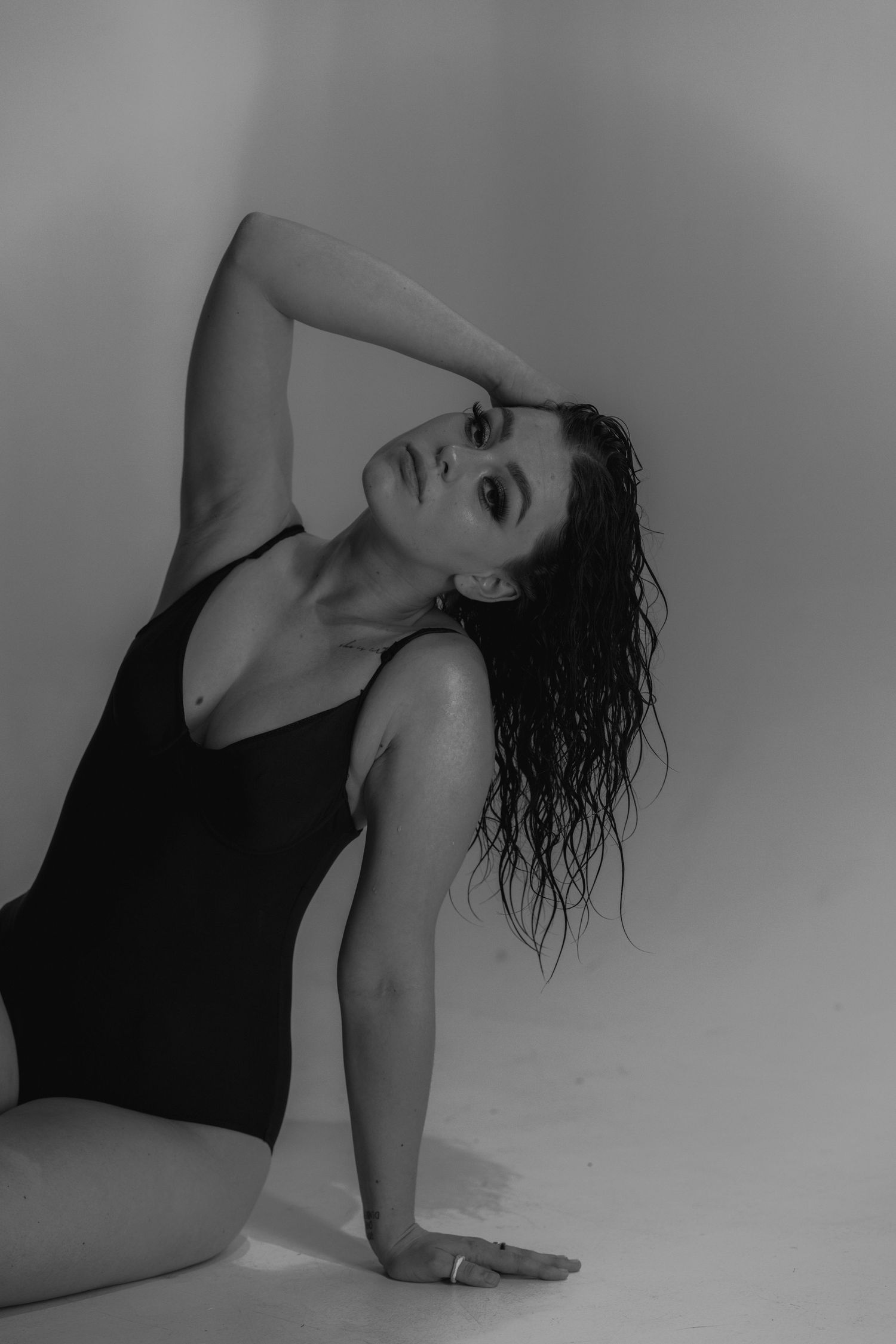 Black and white artistic portrait of a person in a dark leotard posing with wet hair against a light backdrop.