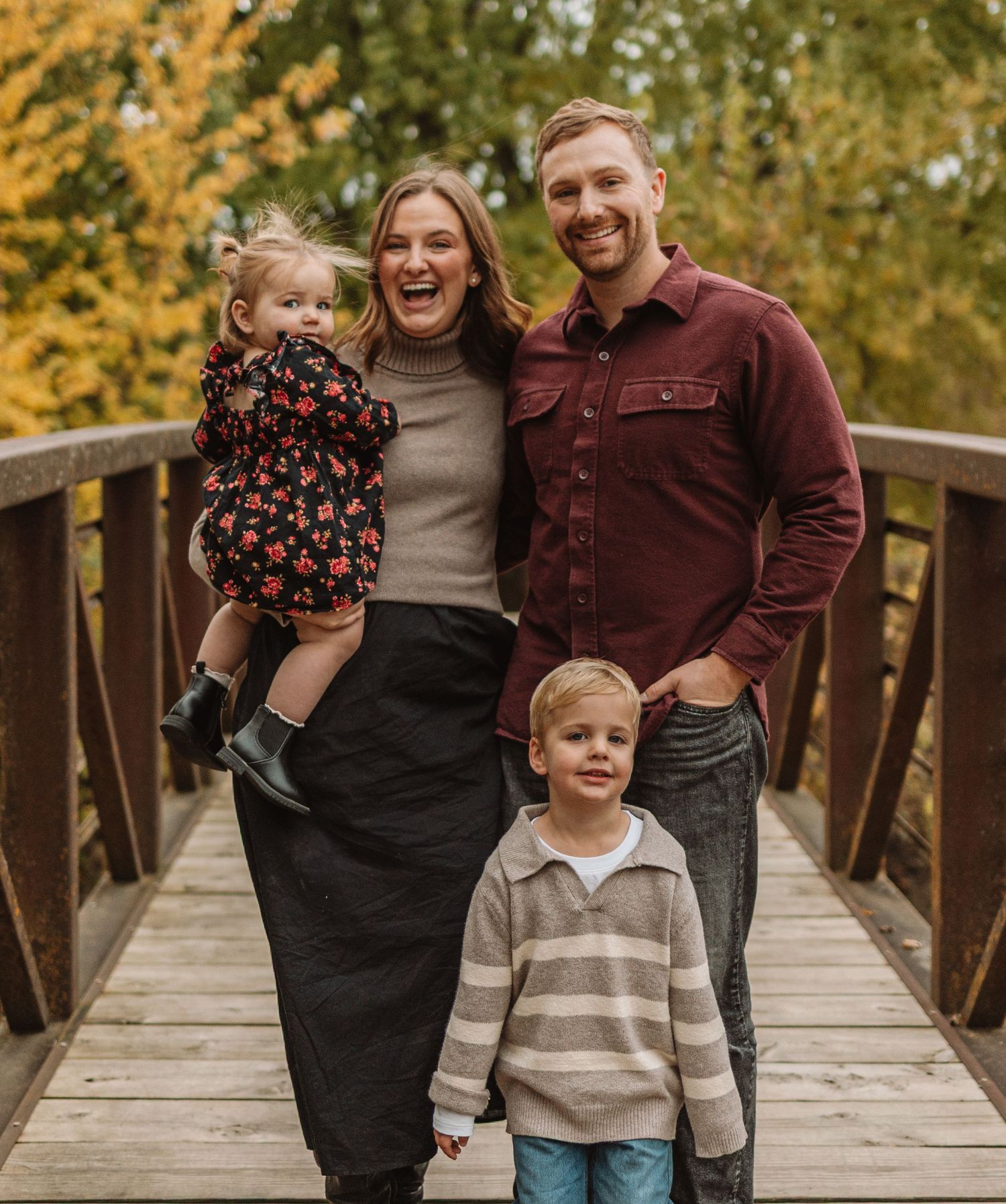 Family shares joyful moments together during autumn photo session on wooden bridge with golden foliage backdrop.