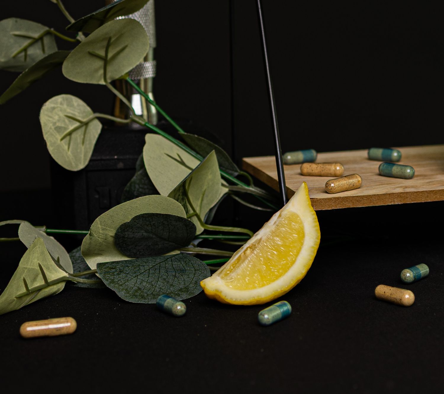 A sliced lemon with green eucalyptus leaves and scattered medicinal pills on a dark background.
