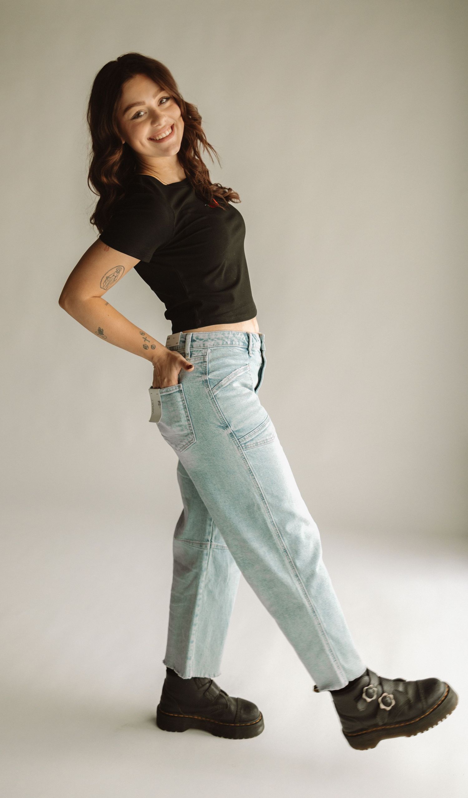 A person wearing a black crop top and light wash jeans poses stylishly against a neutral background in chunky black boots.
