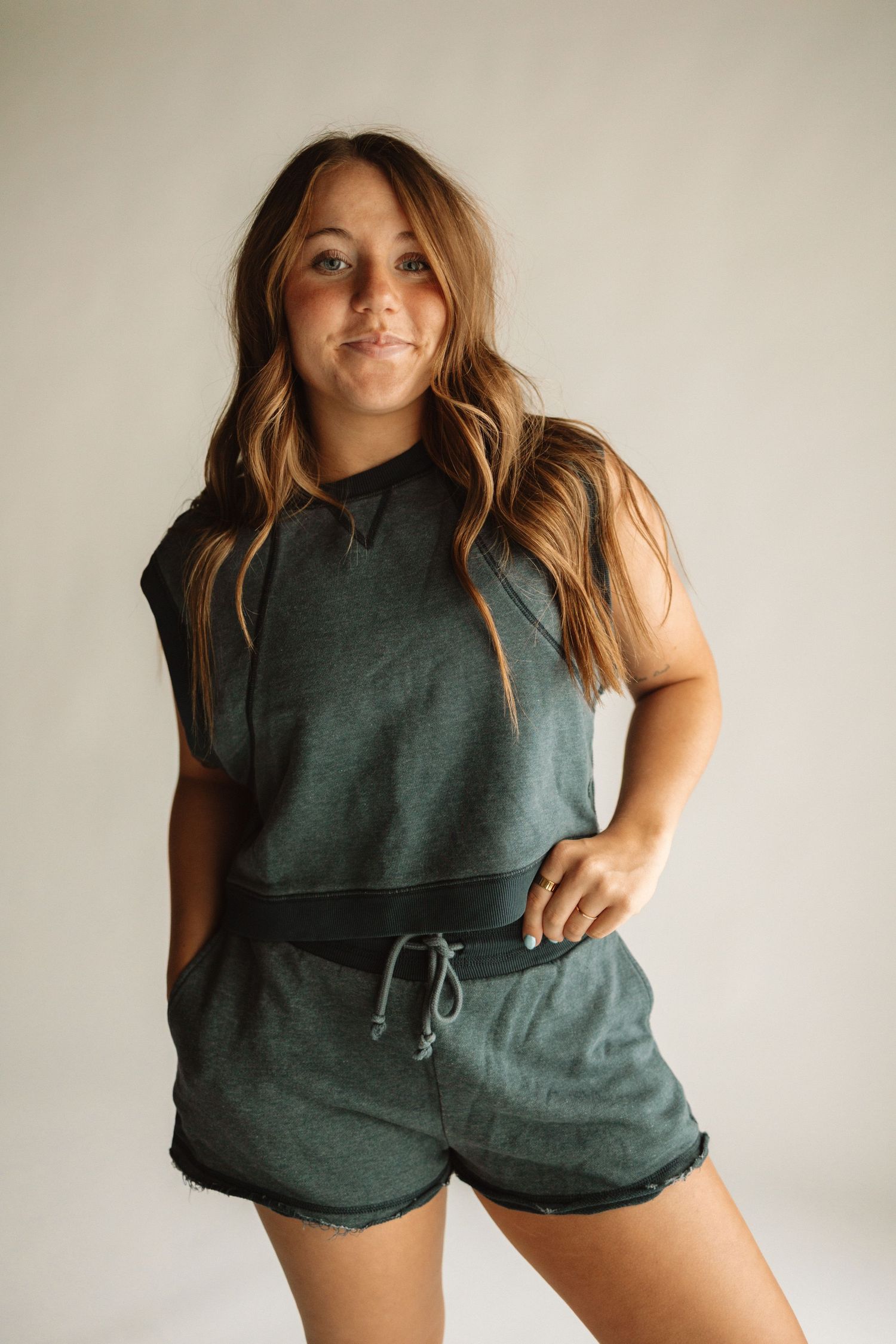 Person wearing a casual green sleeveless top and matching shorts lounges against white wall in relaxed pose.
