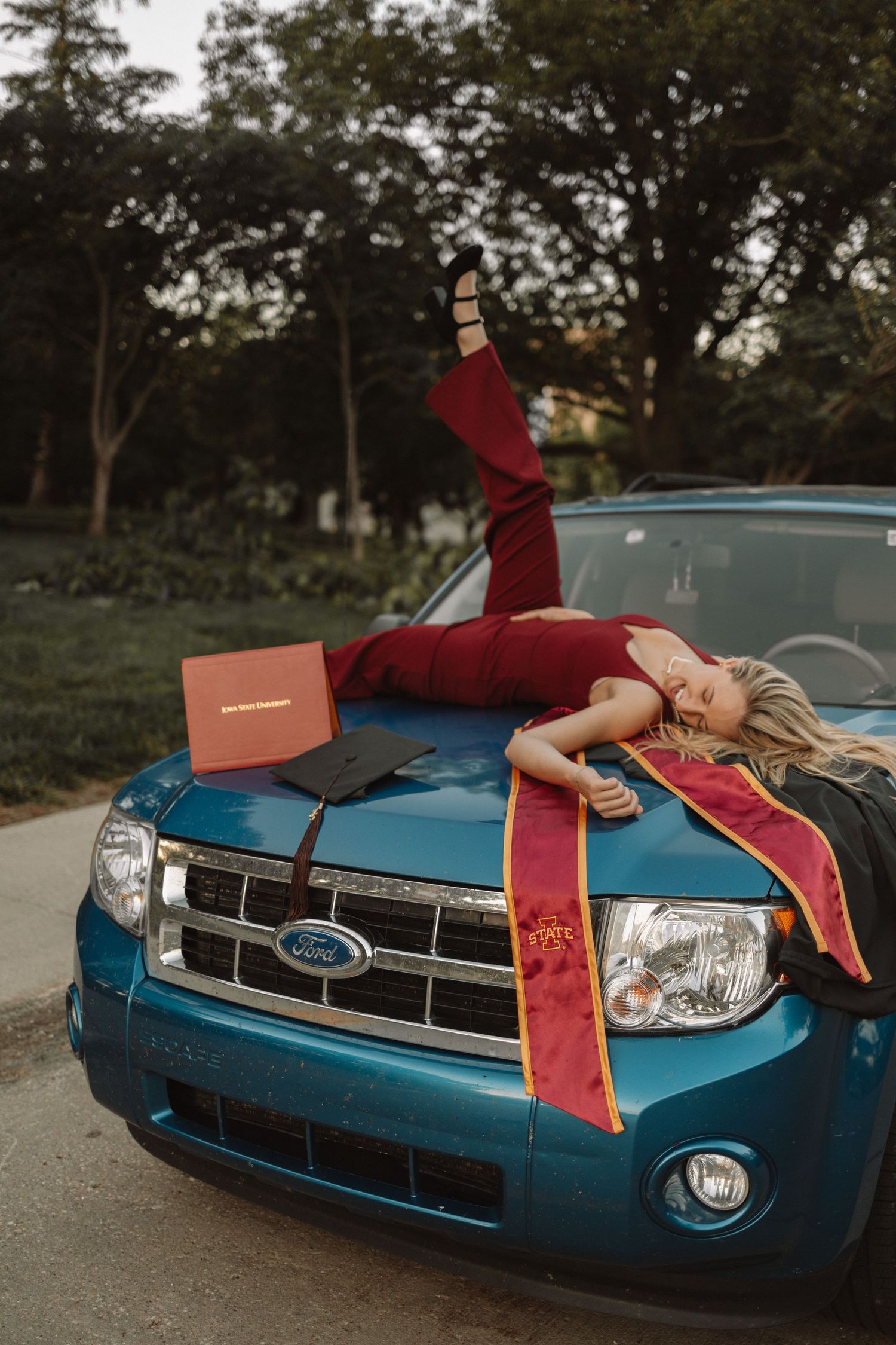 A blue Ford car with red ribbons tied to its hood and roof, photographed at sunset in a parking lot.