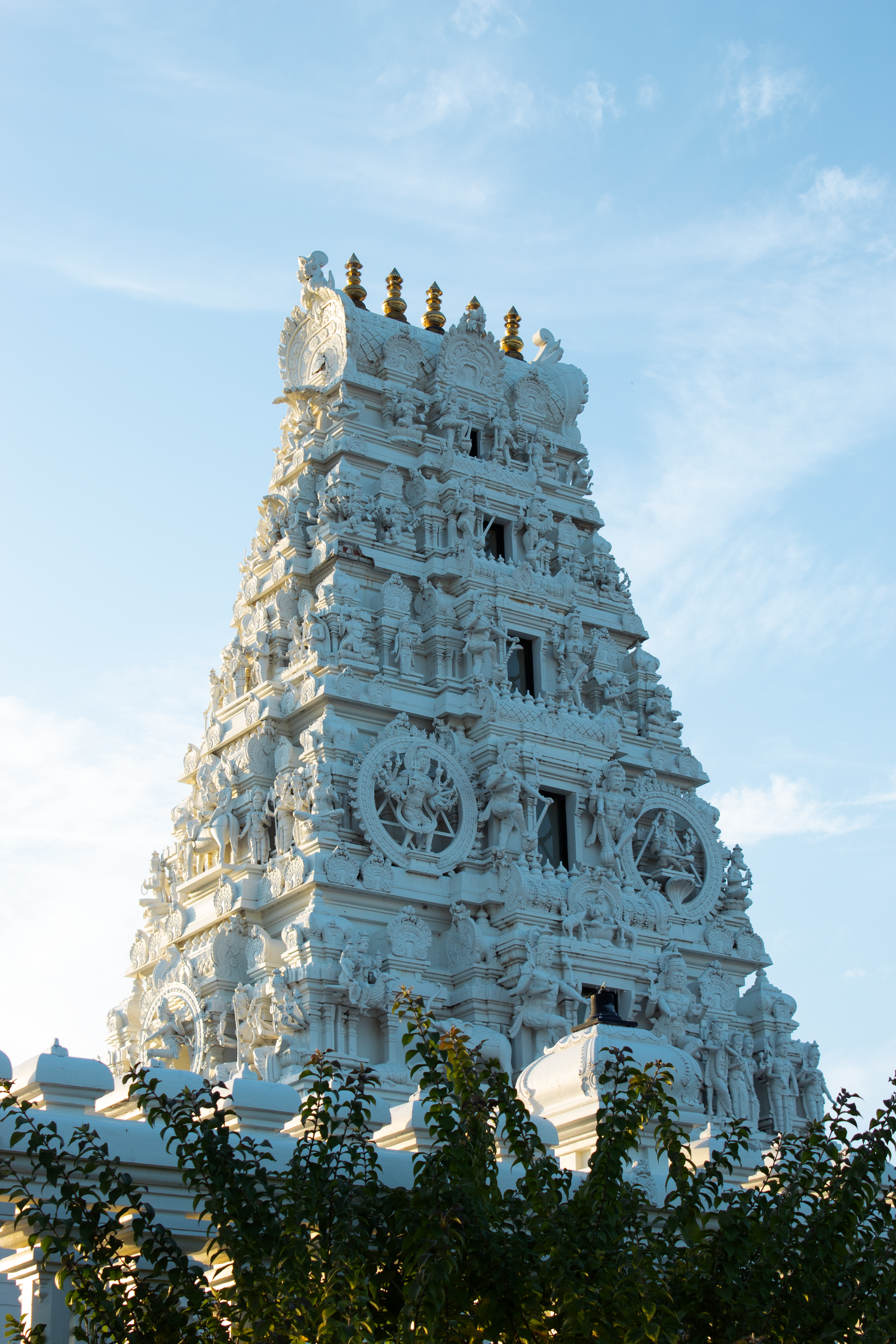 White ornate Hindu temple gopuram with intricate carvings rises against a blue sky at the Sri Venkateshwara Temple in Malibu.
