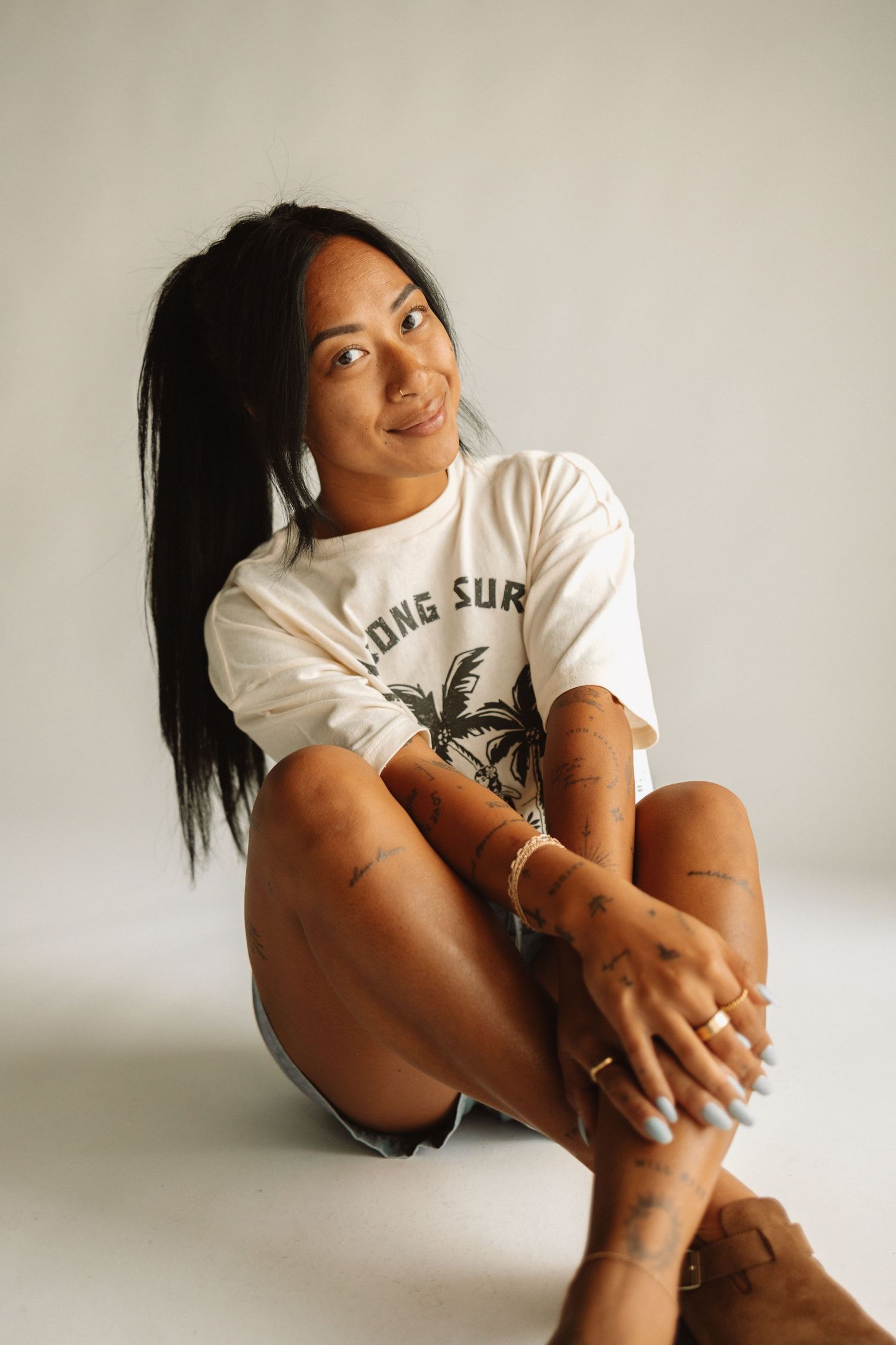 A person in a white graphic t-shirt sits casually against a white wall in a sequence of relaxed poses.