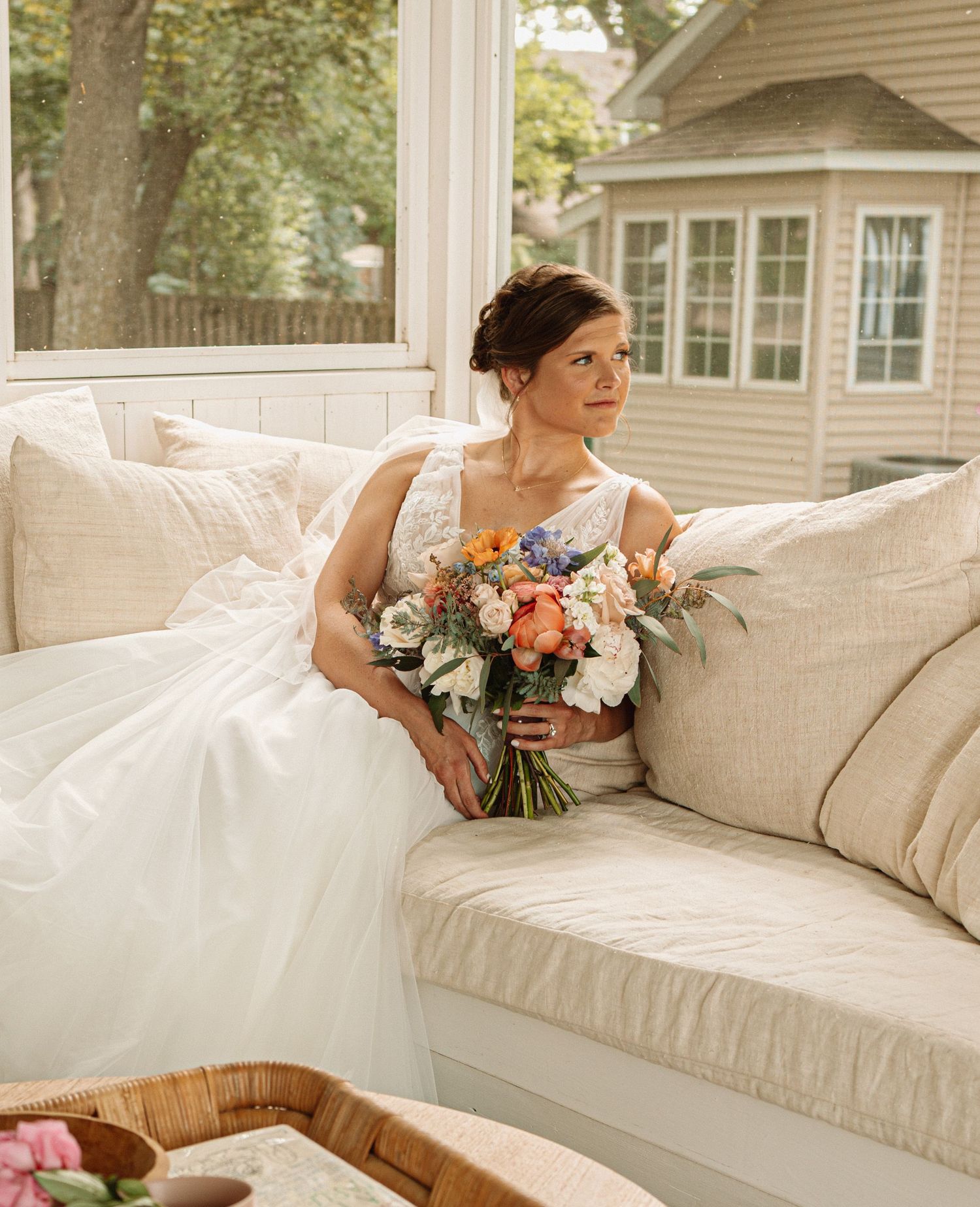 Someone in a white wedding gown lounges elegantly on a cream-colored sofa during a photoshoot sequence.