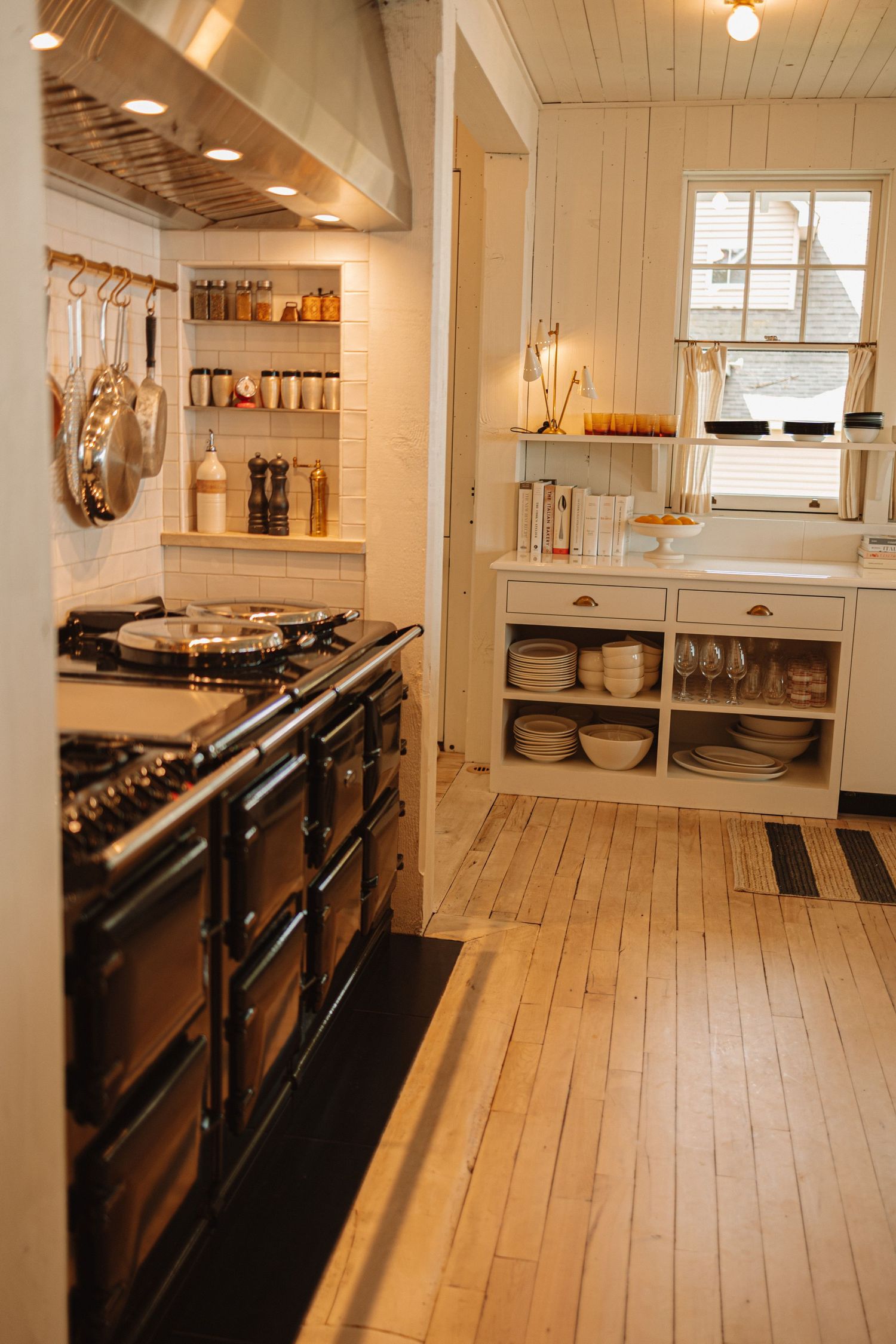 Rustic kitchen interior with wood plank flooring, white walls, and dark display cases creating a bright vintage atmosphere.