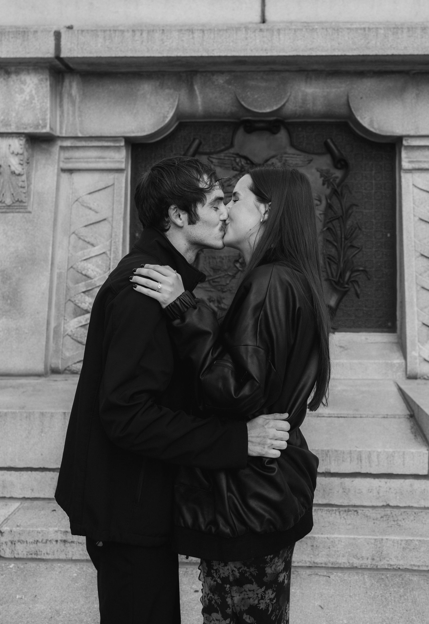 A black and white photo series showing a couple sharing an intimate kiss against an architectural backdrop.