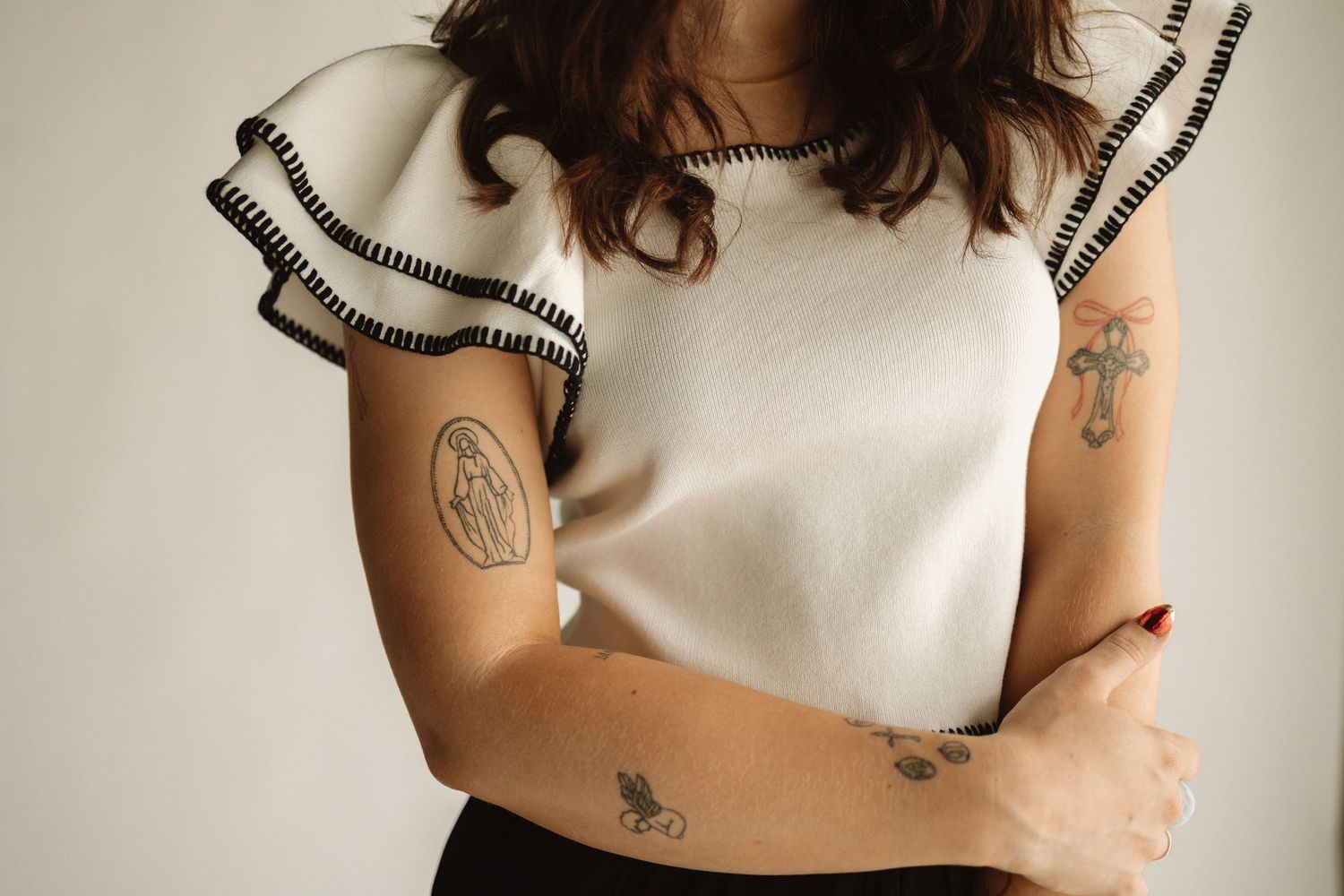 Close up of arms with multiple small tattoos wearing a white top with ruffled short sleeves.