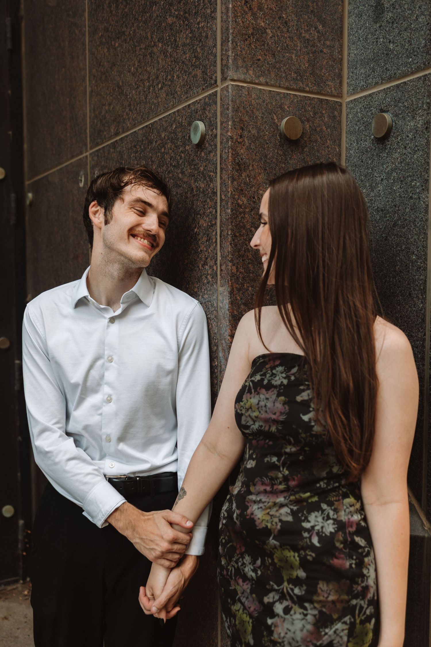 A romantic couple in formal attire shares intimate moments against an industrial concrete wall background.