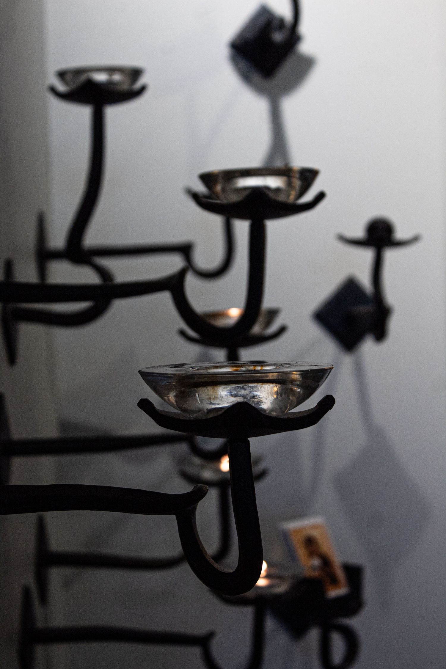 Silhouetted candle holders with metal branches cast dramatic shadows on a light gray wall in moody lighting.