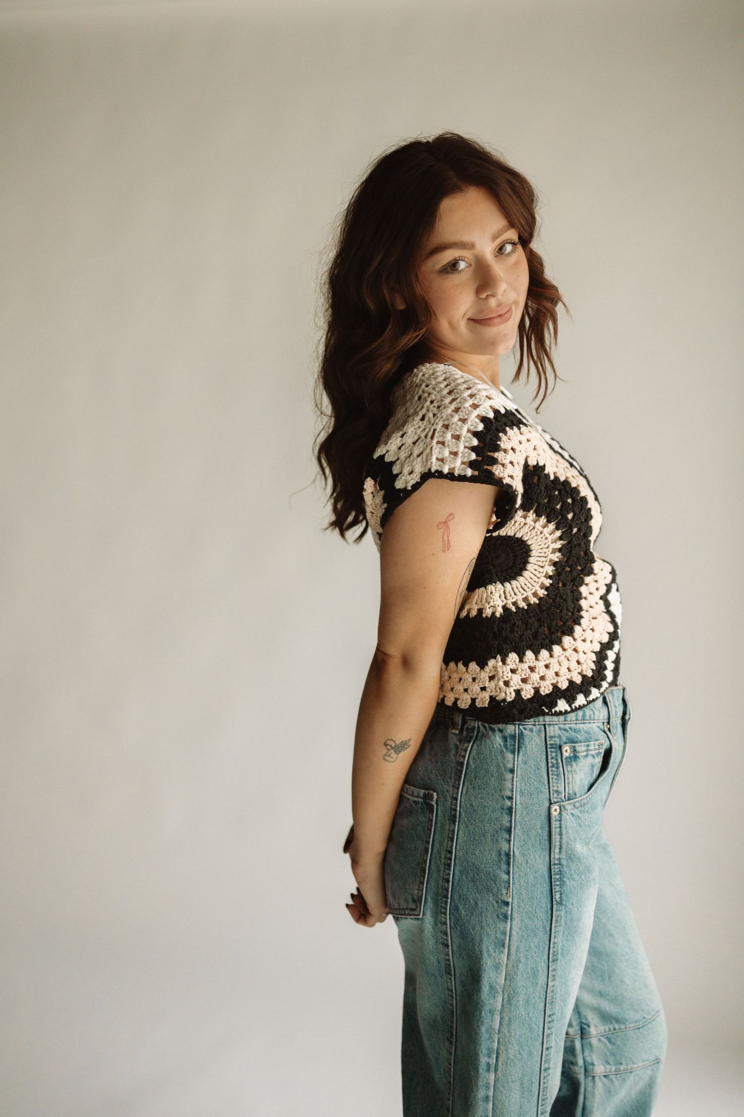 A person wearing a black and white crochet tank top with light wash denim overalls displays the outfit from different angles.