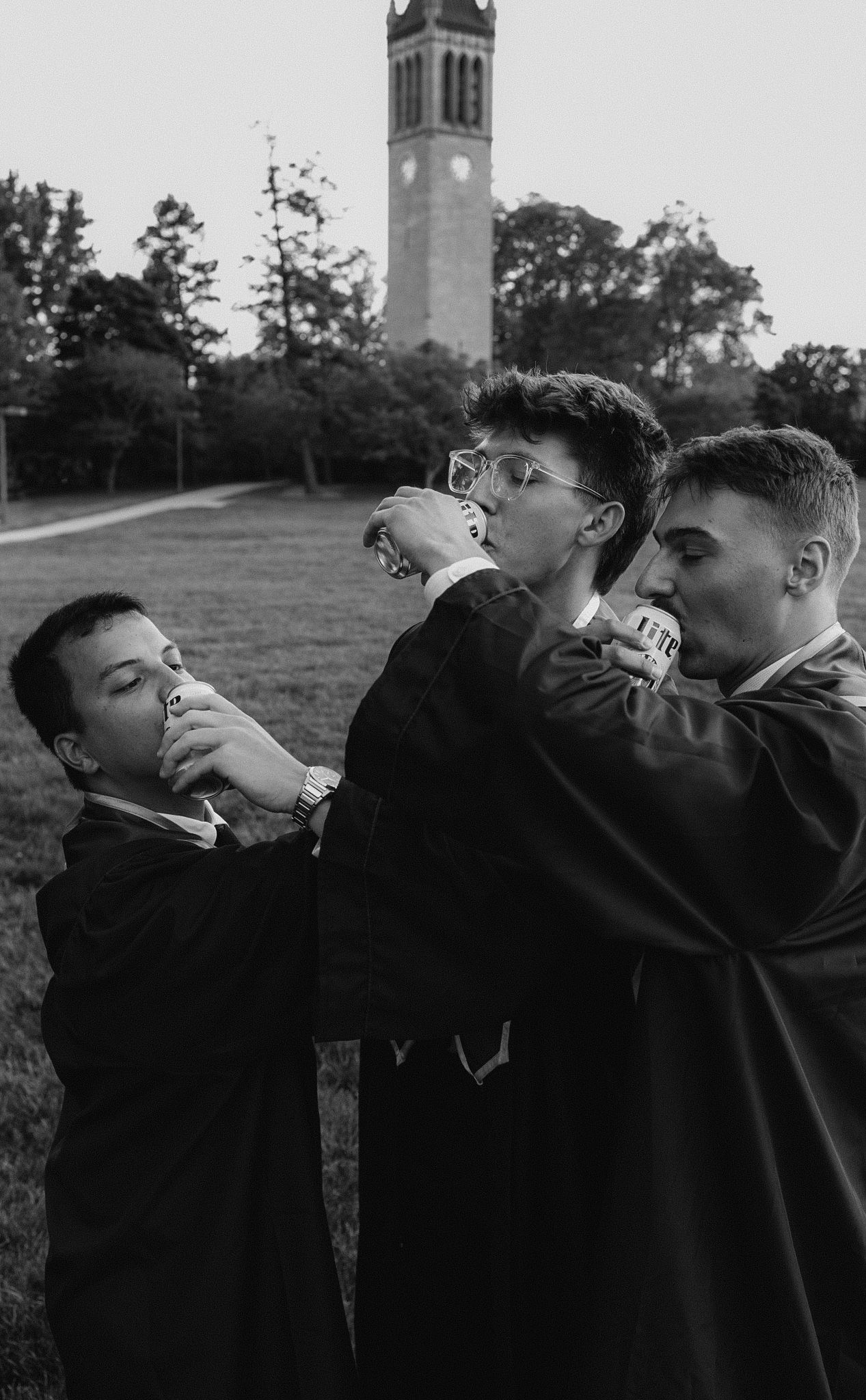 Students in graduation gowns drinking together with a clock tower in background.