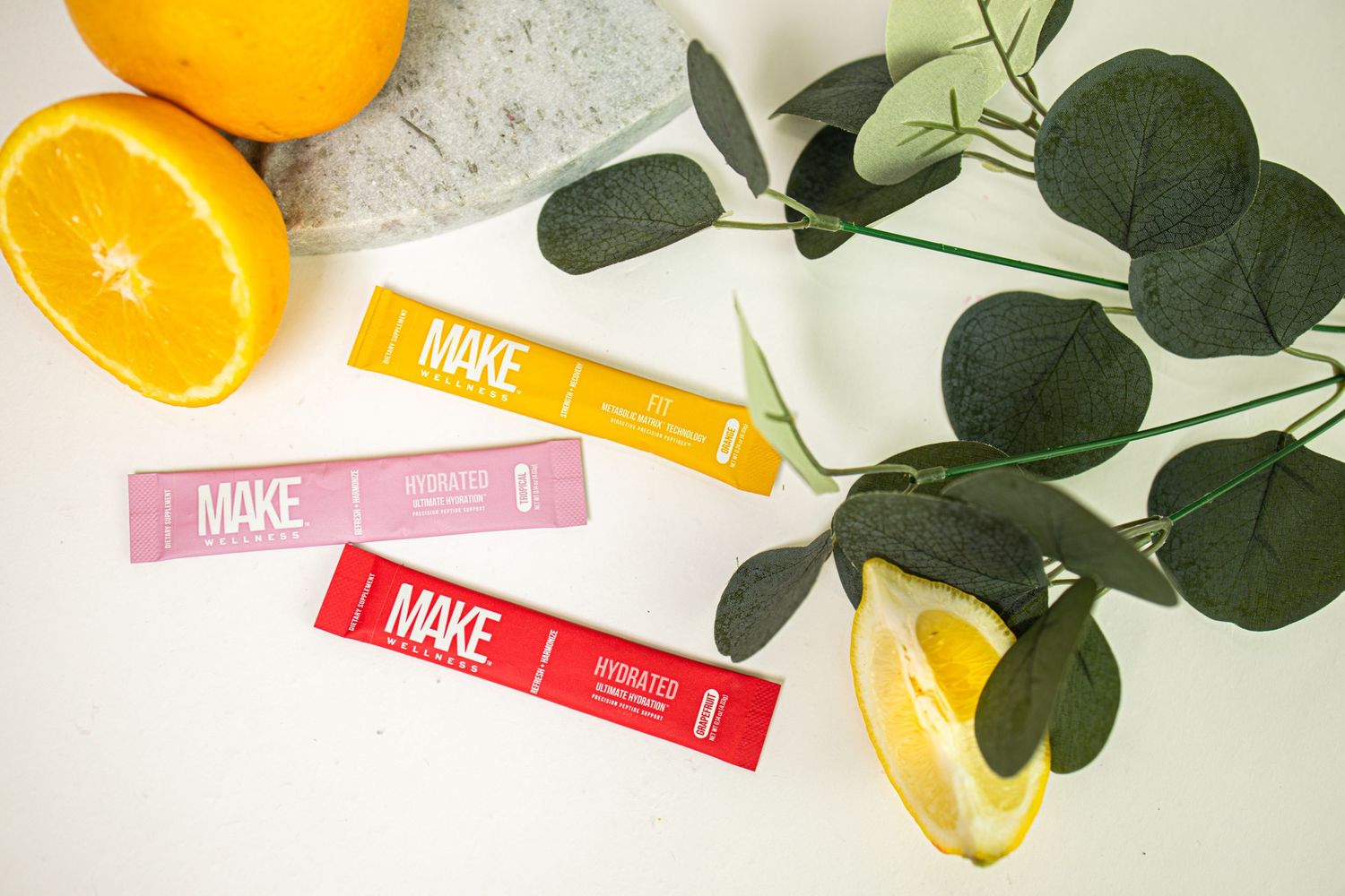 Fresh citrus fruits arranged with green leaves and pink product packaging on a white marble surface.