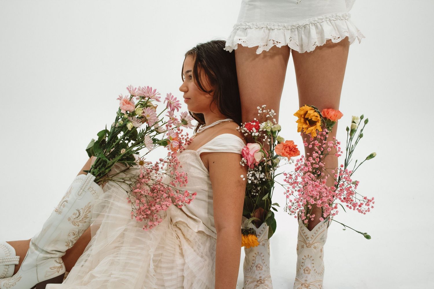 White boots and dress with pink floral arrangements against a light grey studio backdrop.