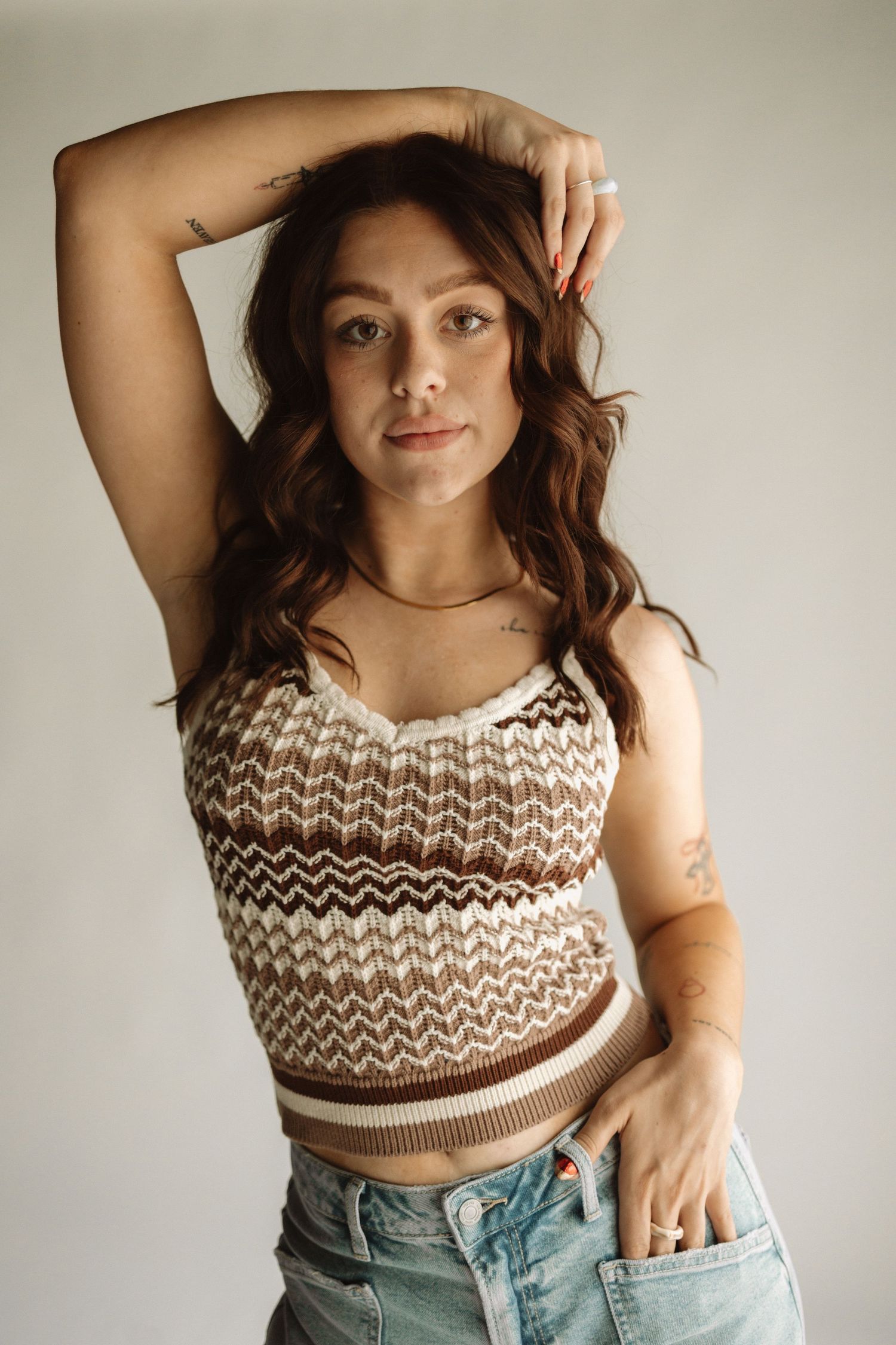 Portrait of model wearing chevron patterned crop top and jeans in natural light studio setting.