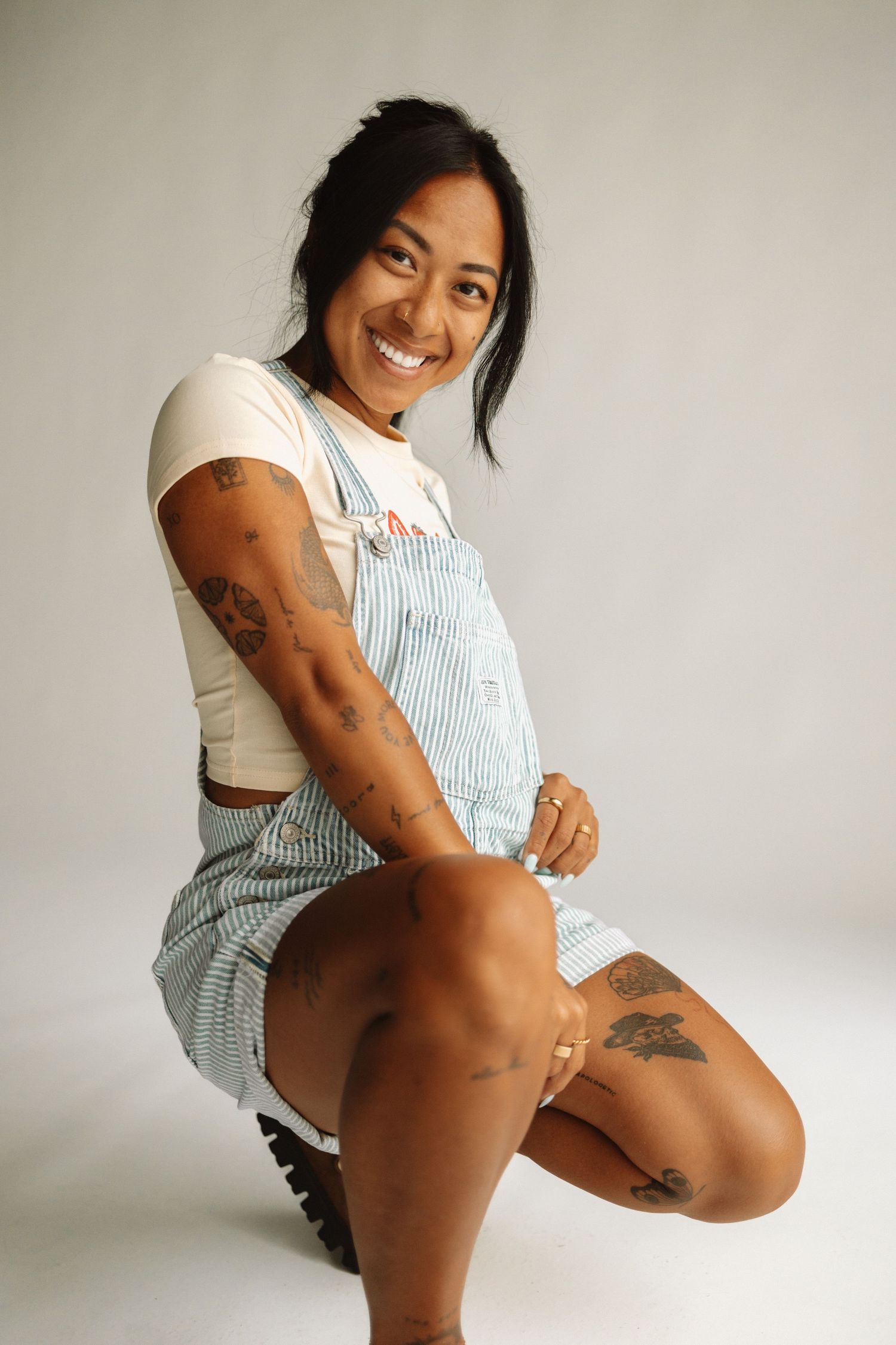 A series of five casual fashion and lifestyle poses against a white wall wearing a striped summer outfit.