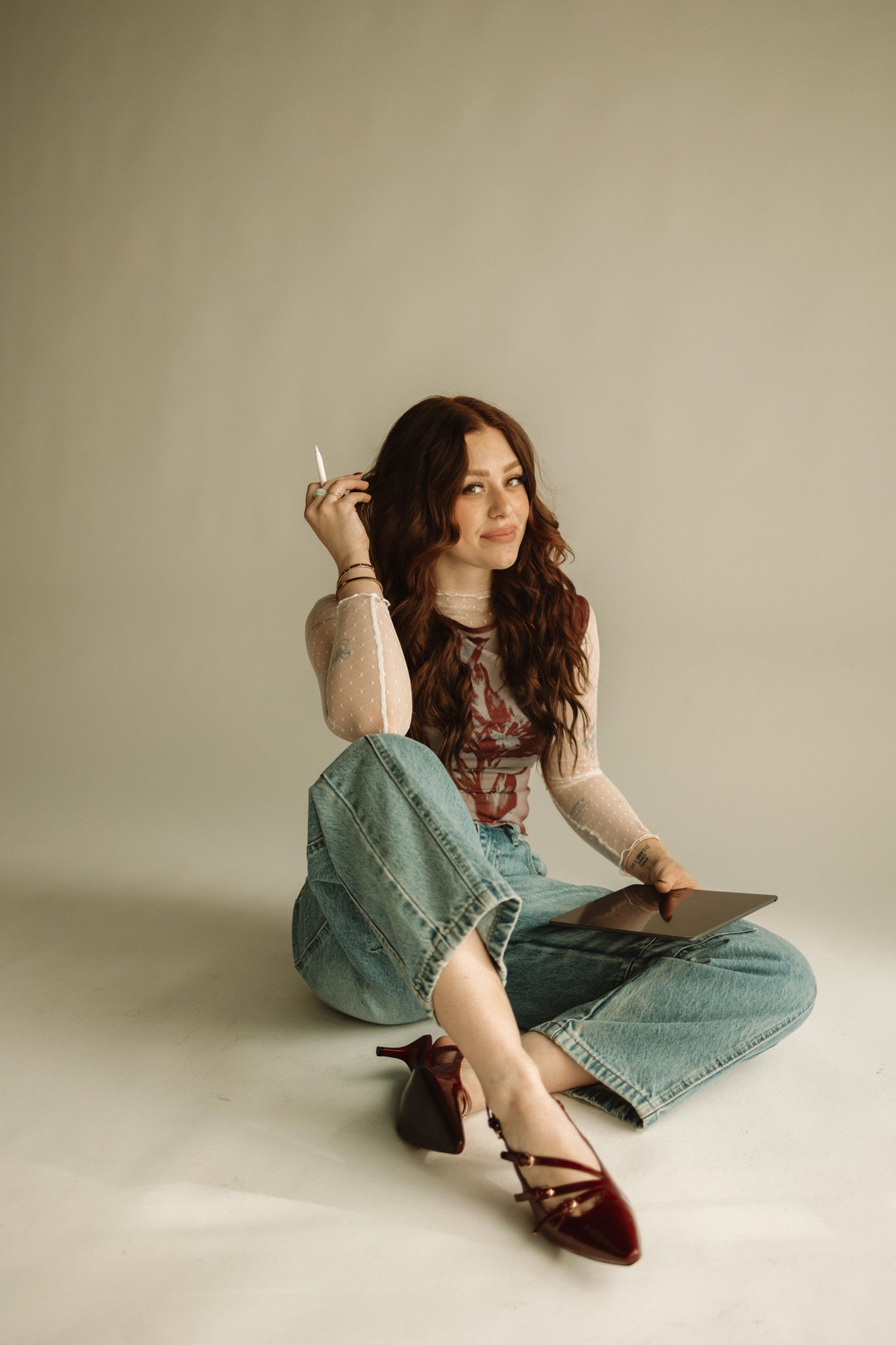 A fashion model wearing a denim jumpsuit and red shoes poses on a light backdrop in a lifestyle photoshoot series.