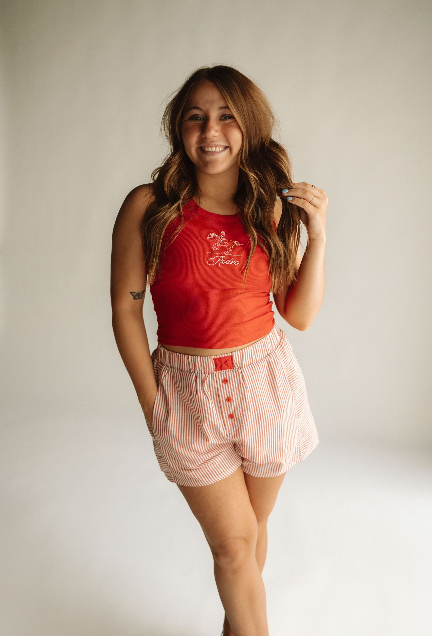 Person wearing a red tank top and pink striped shorts poses against a white background in a casual summer outfit.
