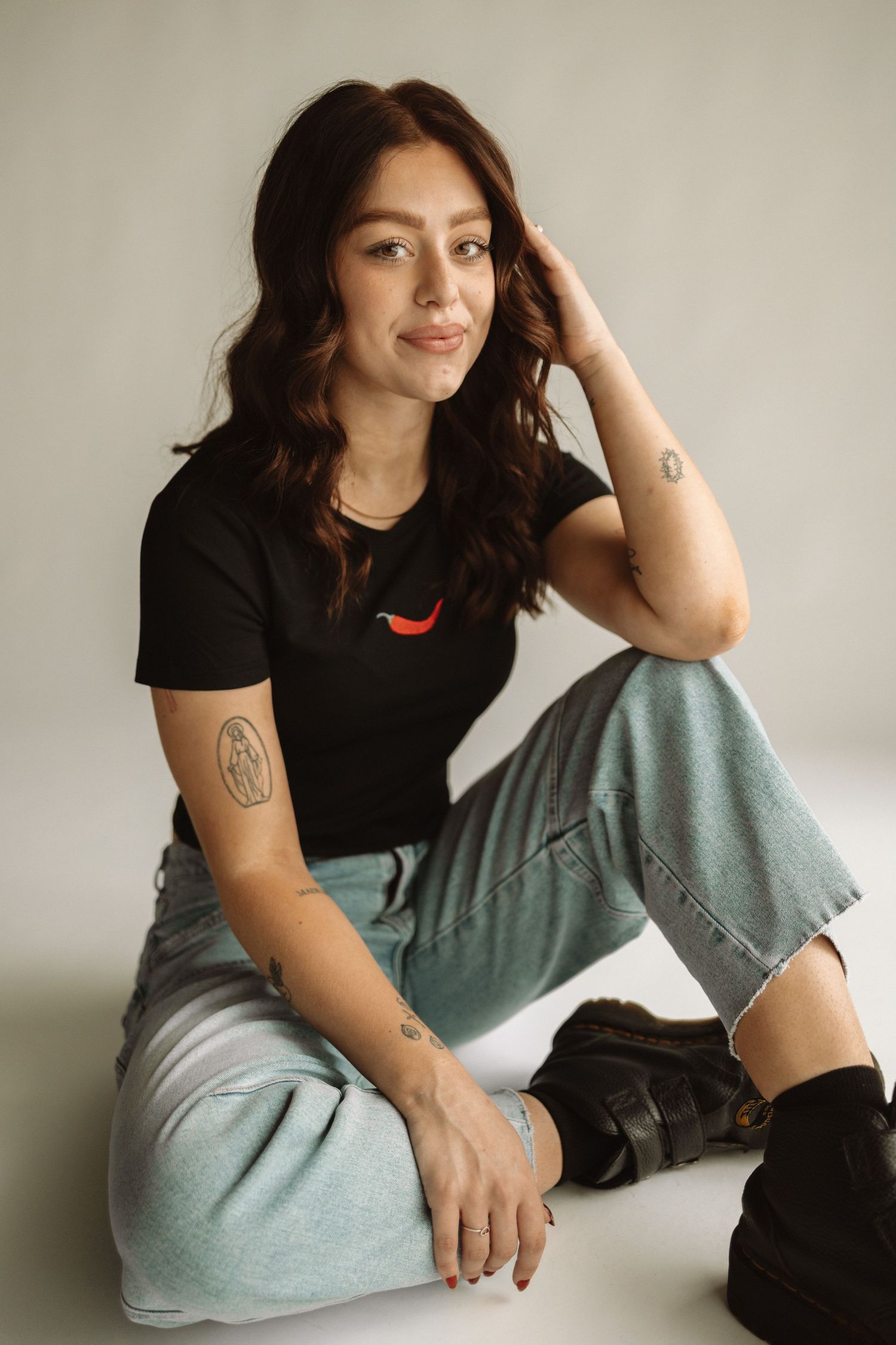 Person in black t-shirt and light gray pants sits casually against white wall in multiple relaxed poses.