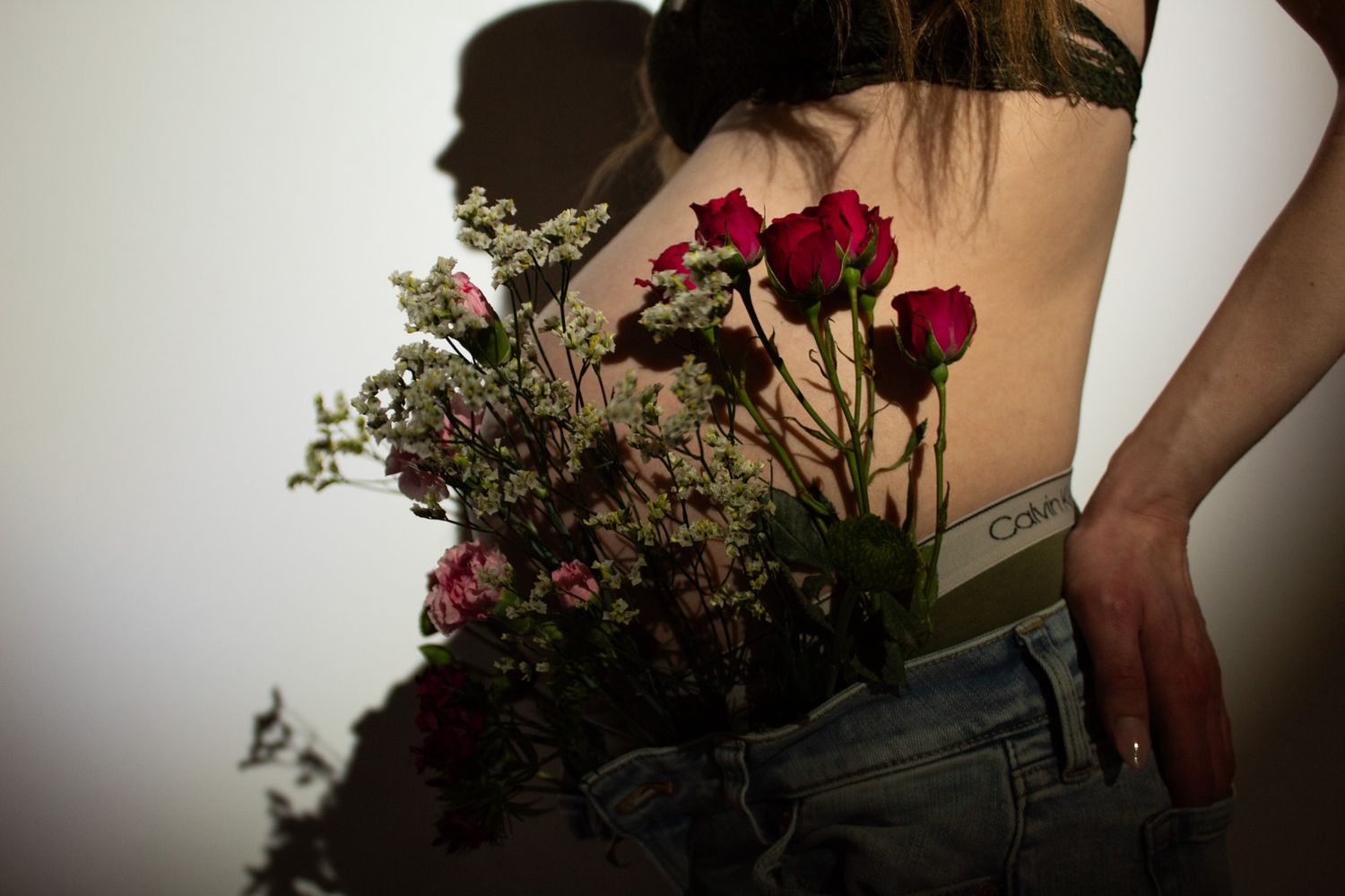 Artful shot of red roses and delicate flowers against midriff wearing denim jeans in moody lighting.