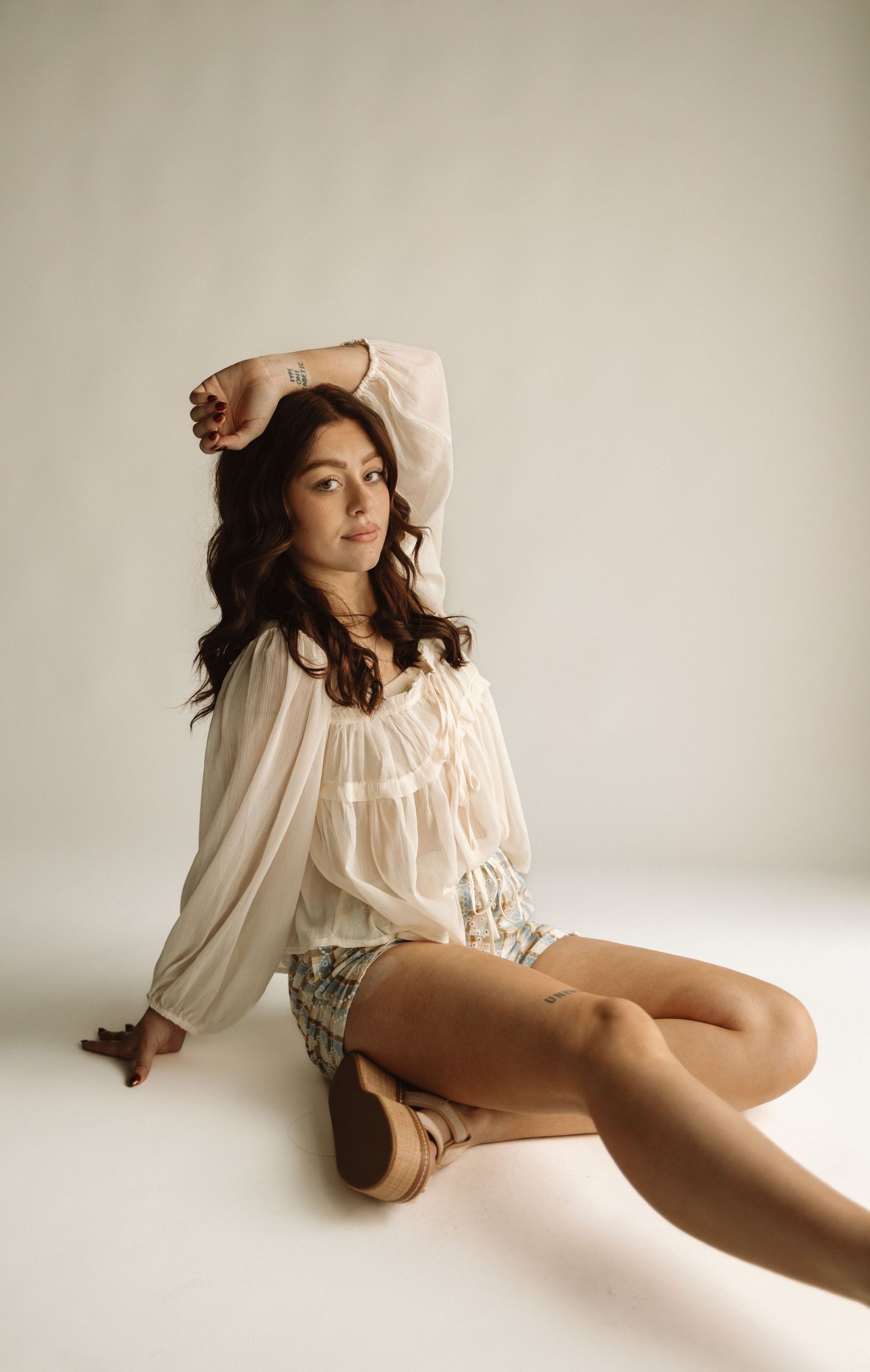 A model in a cream-colored peasant blouse and floral shorts poses against a white backdrop in a vintage-inspired photoshoot.