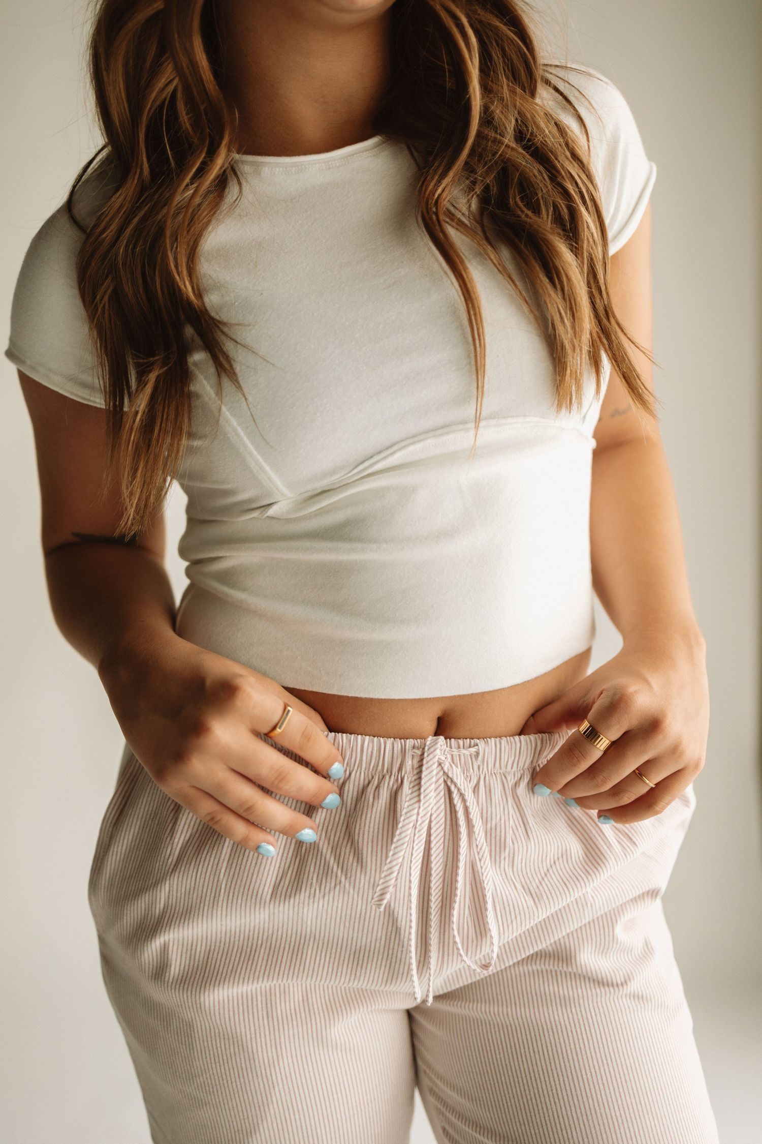 Person wearing a white crop top and beige striped drawstring lounge pants in a casual indoor setting.