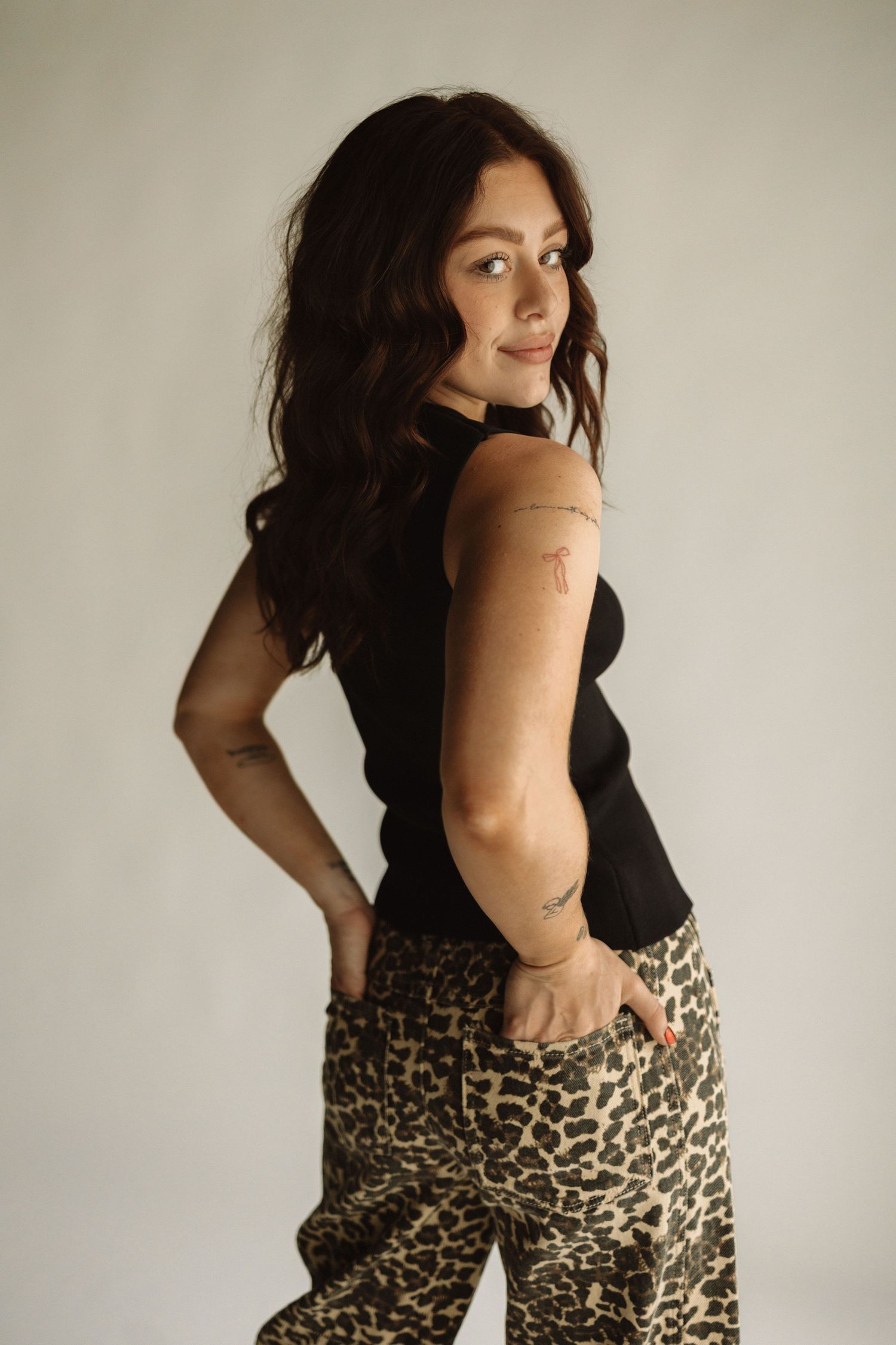 Stylish woman poses against white wall wearing black top and leopard print pants in fashionable outfit.