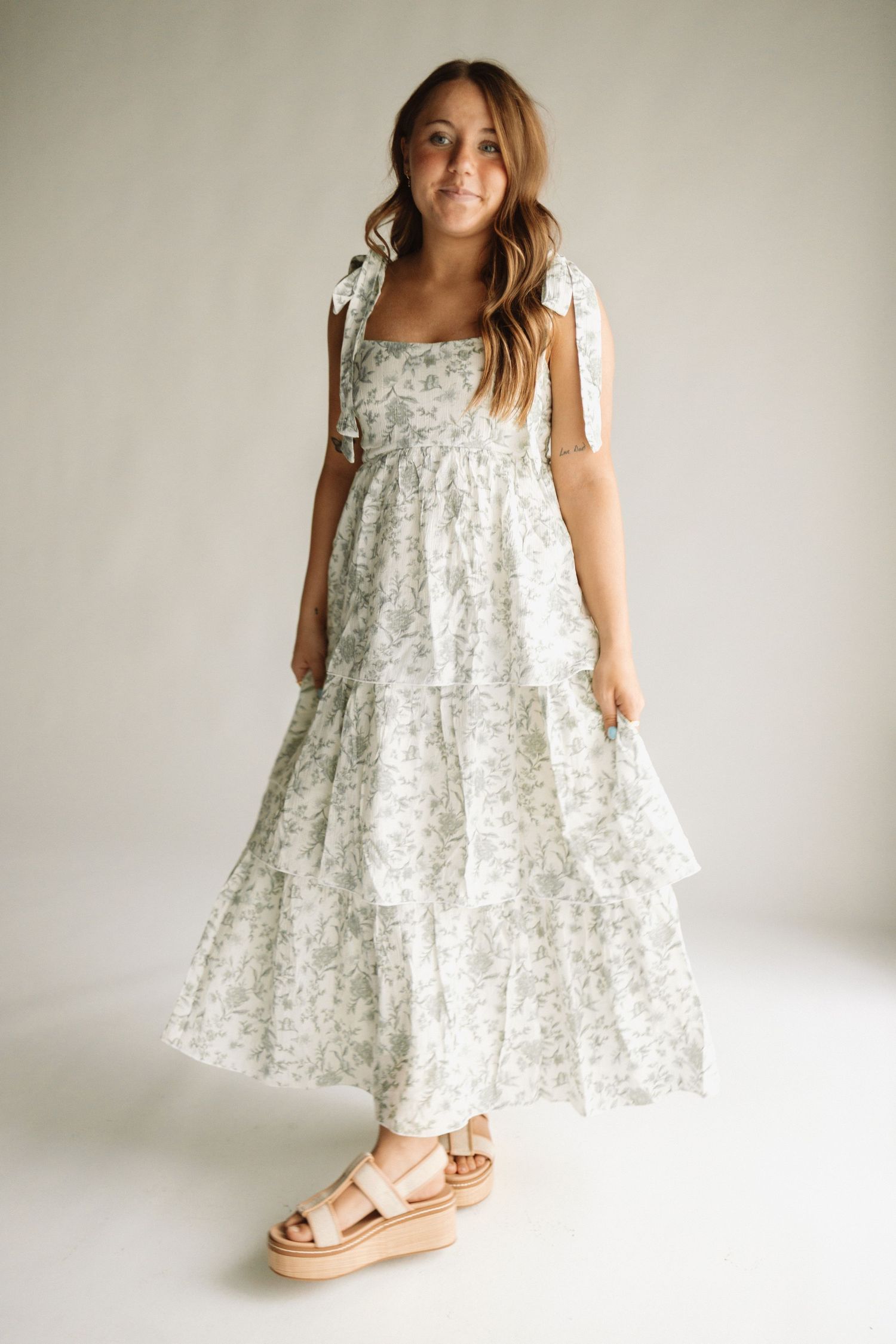 A stylish summer dress in white and grey floral print with tiered ruffles and tie straps, paired with platform sandals.