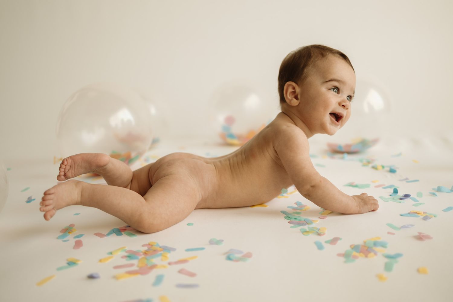 A baby lies on their back while crawling across a white surface decorated with soft pastel-colored floral patterns.