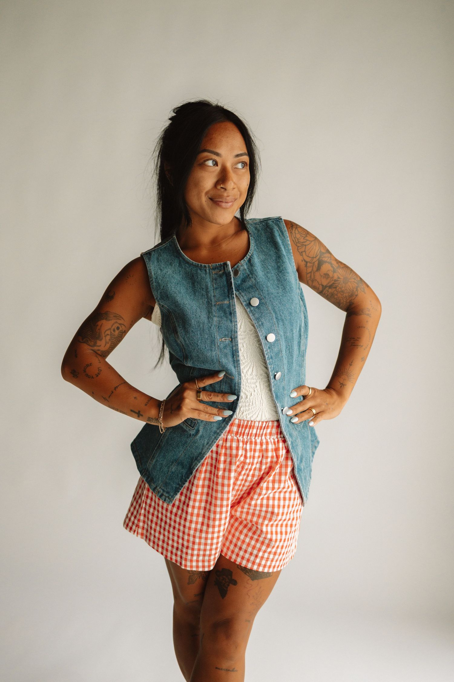 Denim vest styled with red gingham shorts and white top in casual summer photoshoot.