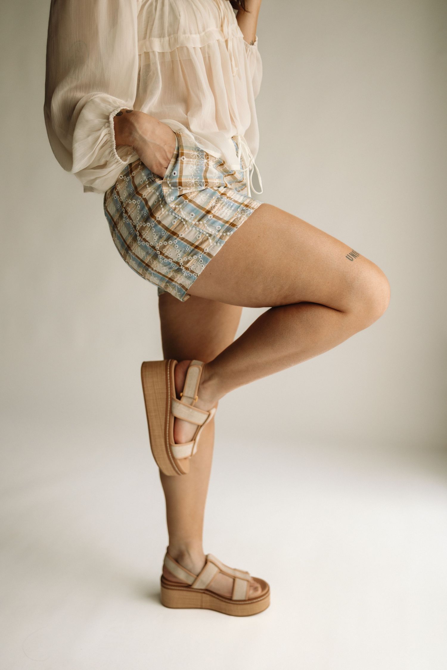 Model wearing beige paperbag shorts and matching top in six dynamic poses showing details and movement of clothing.