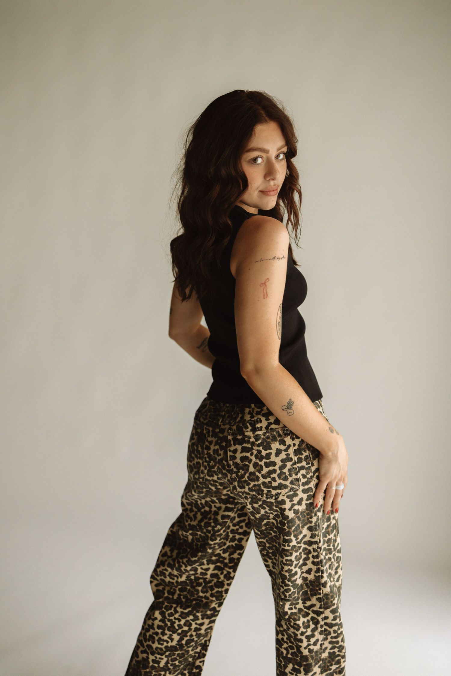 A model poses in a black sleeveless top and leopard print pants against a light backdrop in a studio setting.