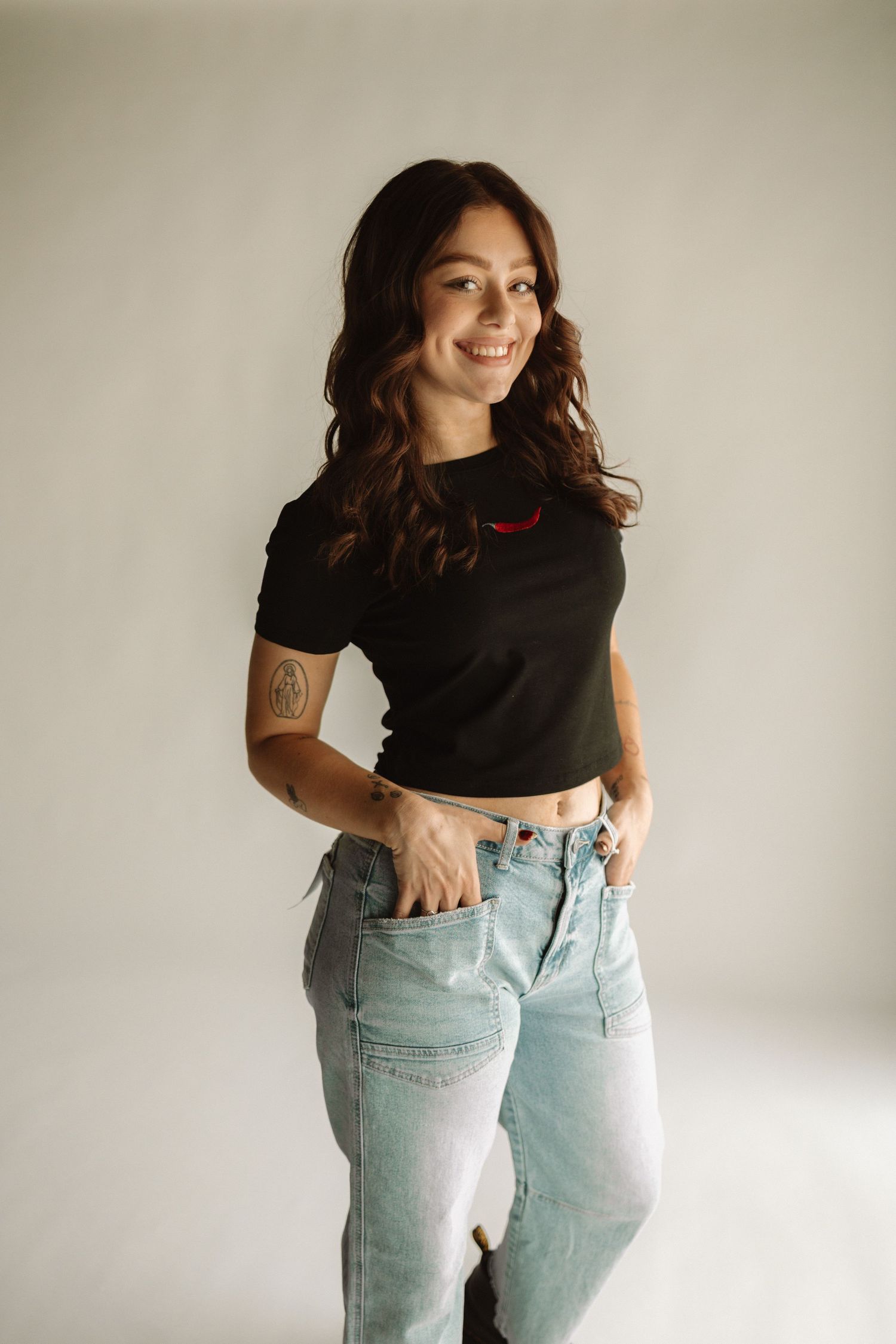 A fashion photo series showing a person wearing light wash high-waisted jeans and a black crop top against a white wall.