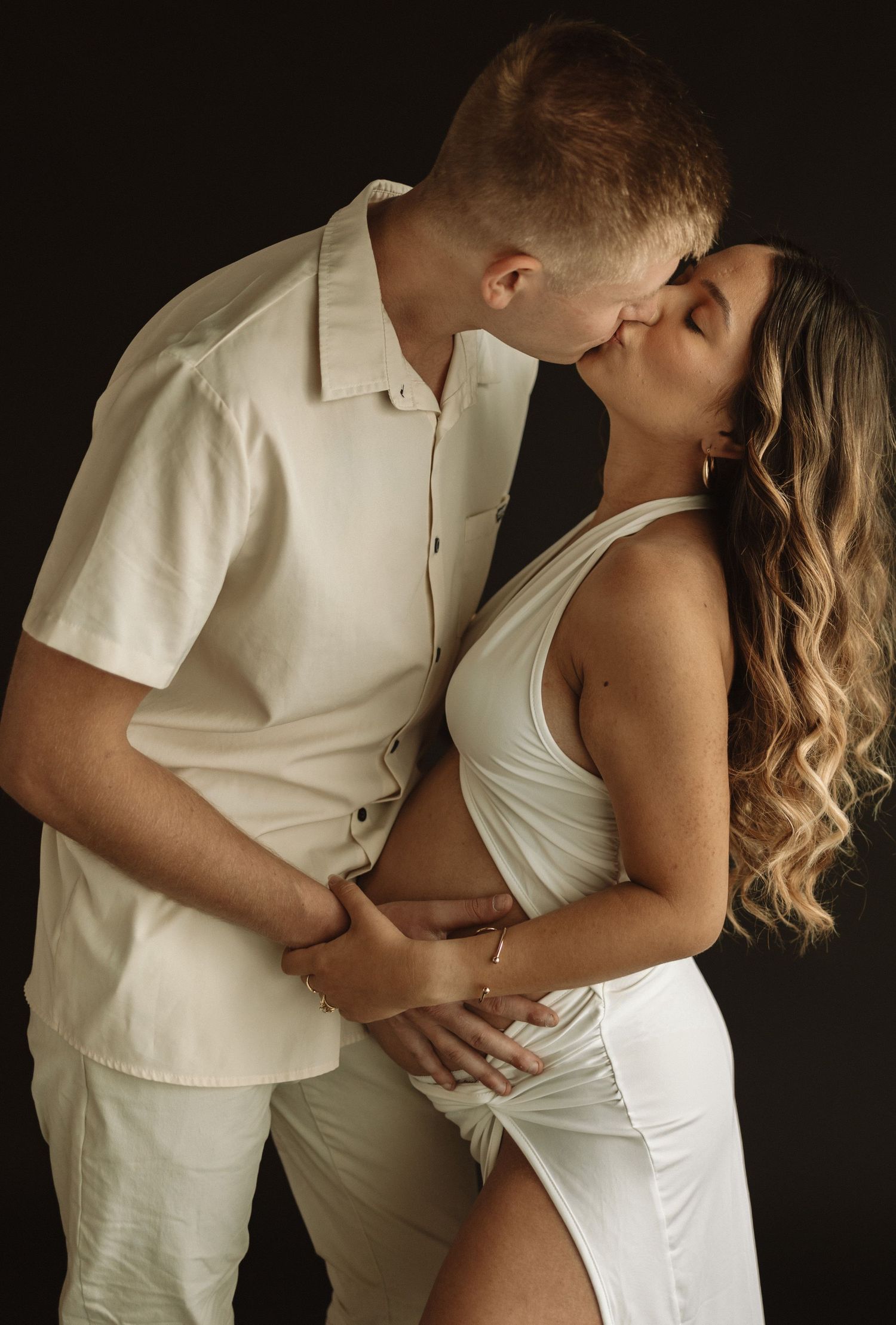 Artistic black and white maternity photo series showing couple in matching white outfits embracing in intimate poses.