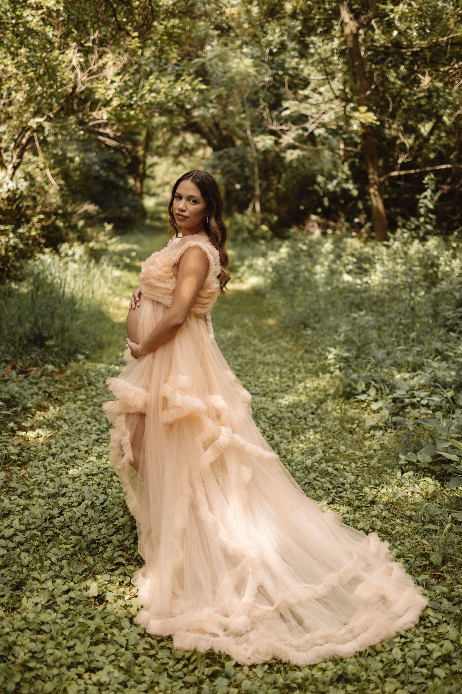 A flowing peach tulle dress swirls gracefully in a sunlit garden setting with lush greenery and natural light.