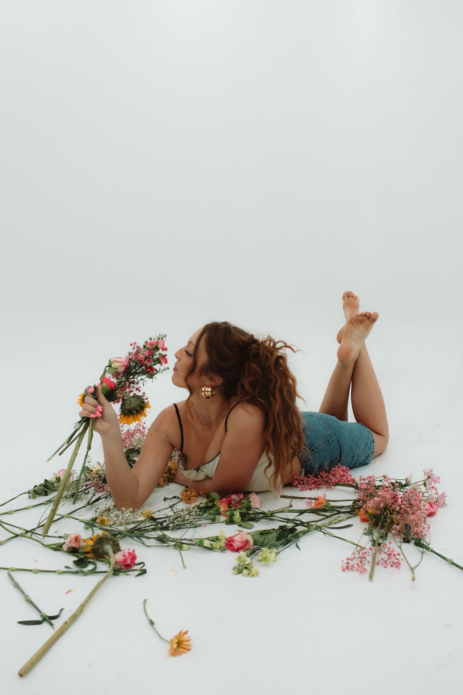A figure laying on white background with scattered colorful flowers and greenery creating a romantic spring scene.