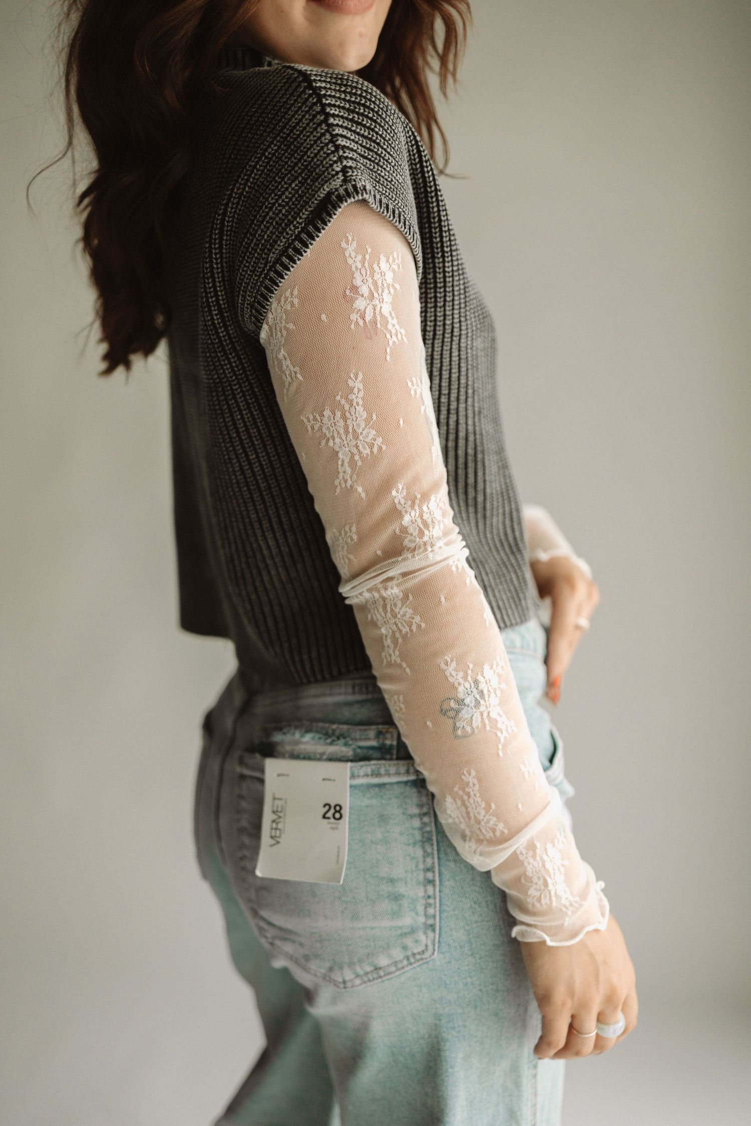 Stylish outfit featuring a dark knit sweater with delicate white lace mesh sleeves and light wash denim jeans.