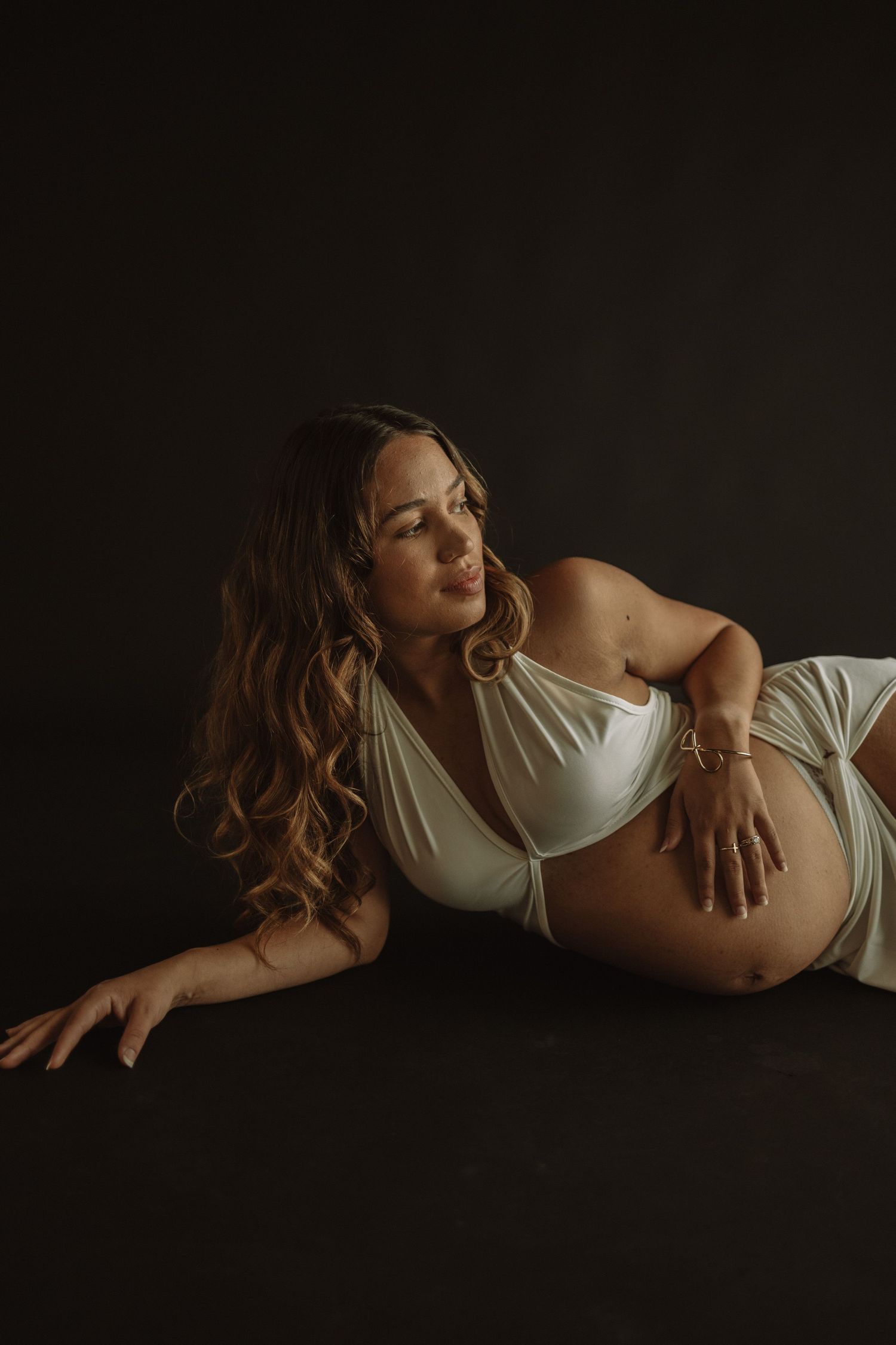 A series of intimate maternity portraits showing a pregnant woman in white lingerie against a dark background.